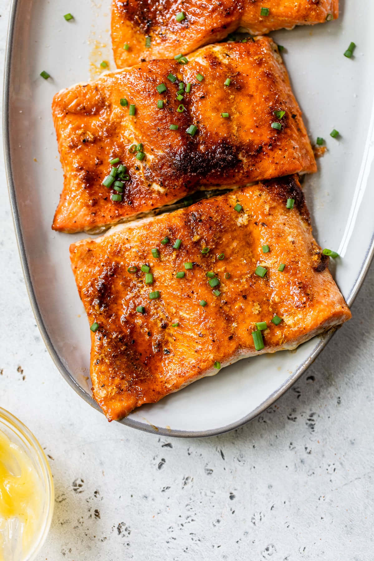 Salmon 桌布 壁紙 — 三塊上釉三文魚柳，飾以切碎嘅細香蔥，放喺一個白色碟上，背景係有斑點嘅枱面。