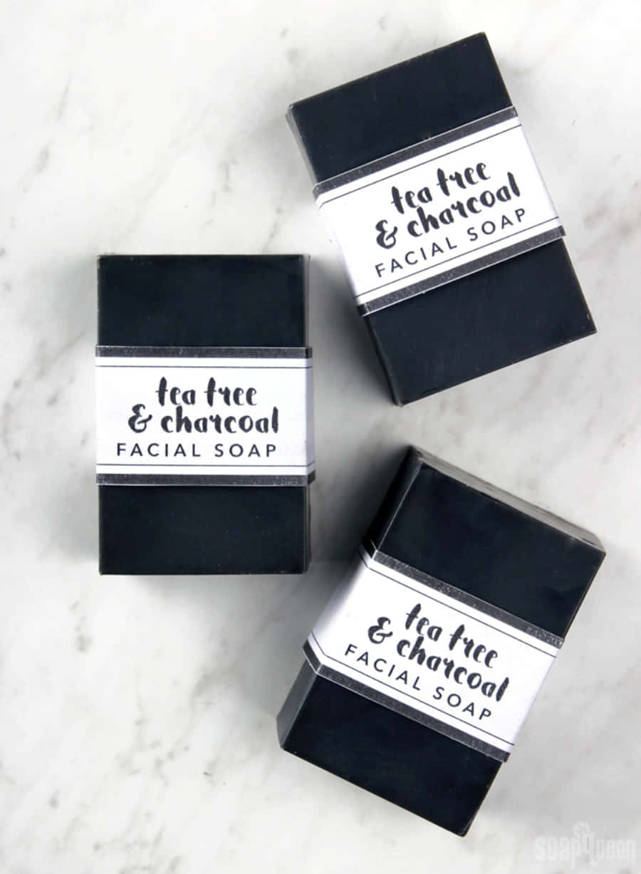 Black Soap 桌布 壁紙 — 三塊帶有白色標籤的啞光黑色茶樹炭洗面皂，放置在乾淨的白色大理石表面上。