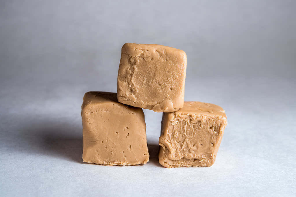 Penuche Fudge 桌布 壁紙 — 三塊焦糖色的軟糖方塊以金字塔形堆疊在柔軟的灰色表面上，帶有柔和陰影。