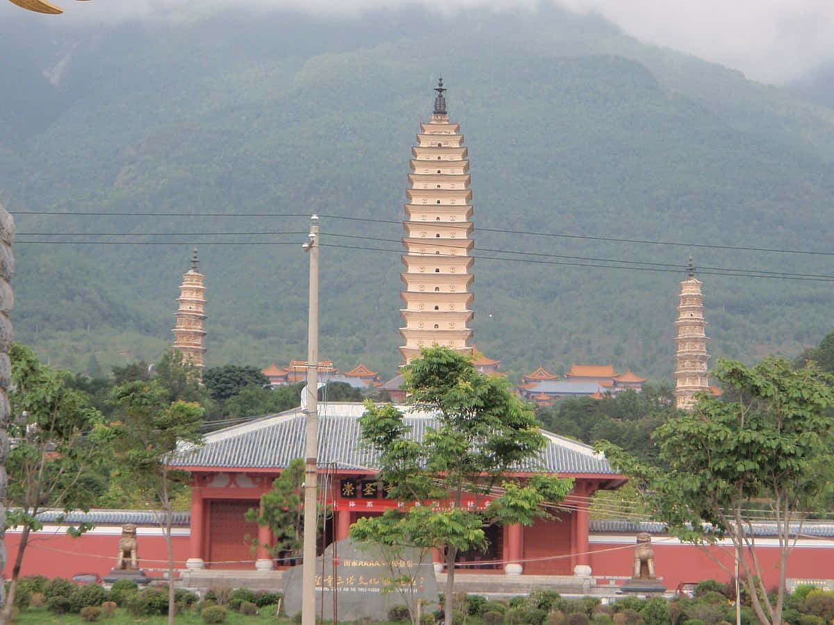 三座塔在紅色寺廟大門後方高高聳立，背景是山巒。