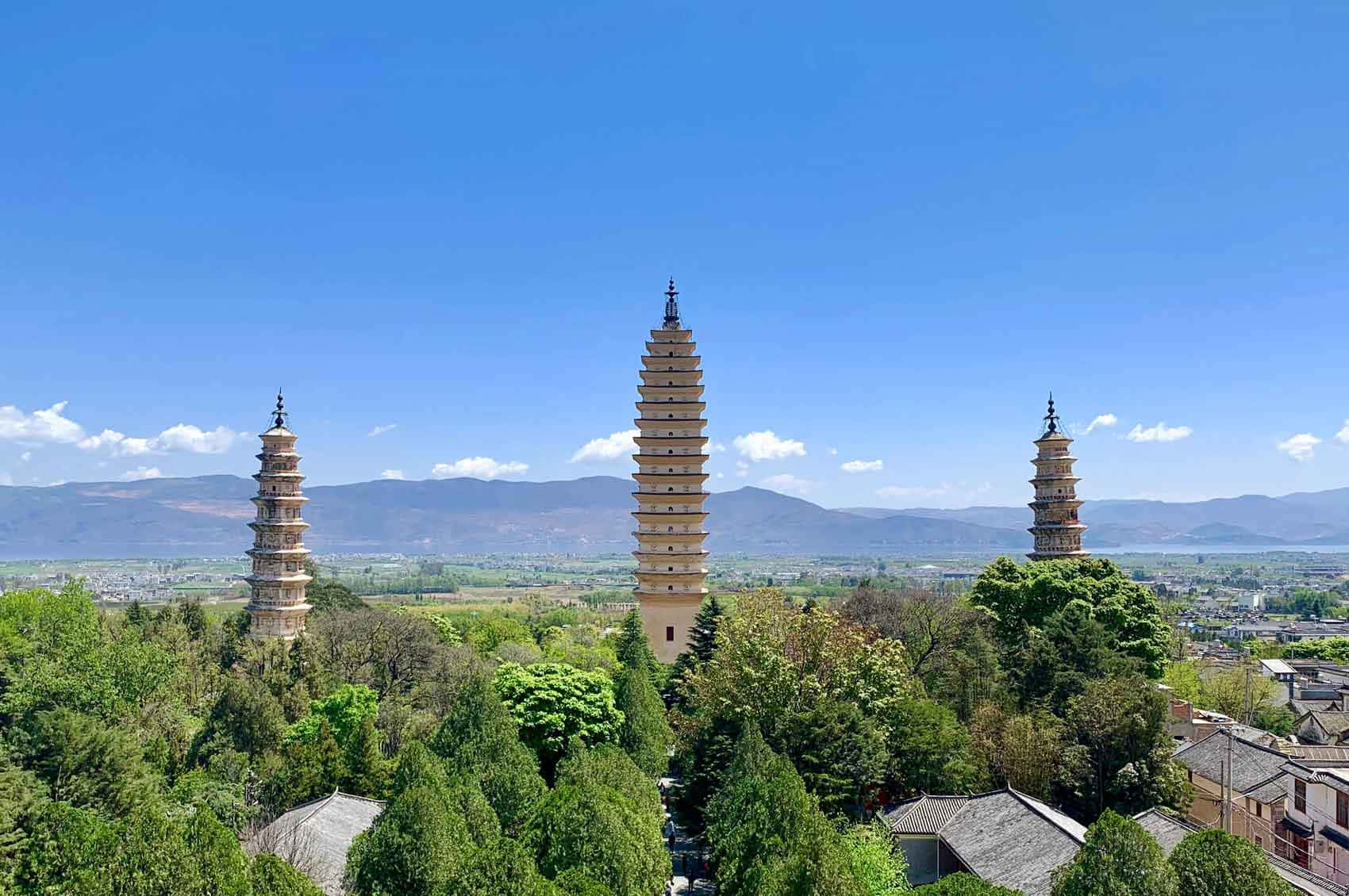 三塔日間風景 壁紙 — 三座古塔在茂密的綠樹上方聳立，映襯著清澈的藍天和遠山。