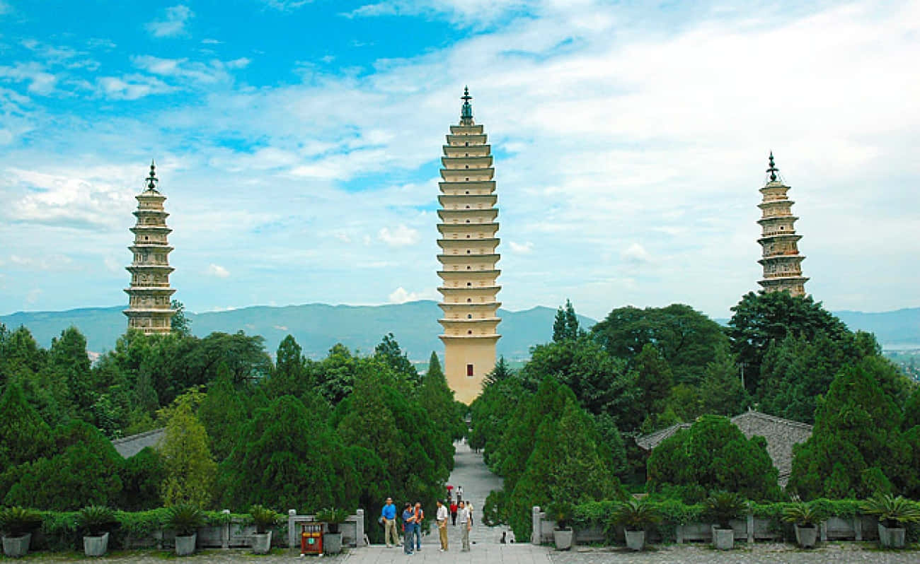三塔與遊客 壁紙 — 三座古老寶塔在茂密綠樹中雄偉聳立，藍天白雲點綴其間。
