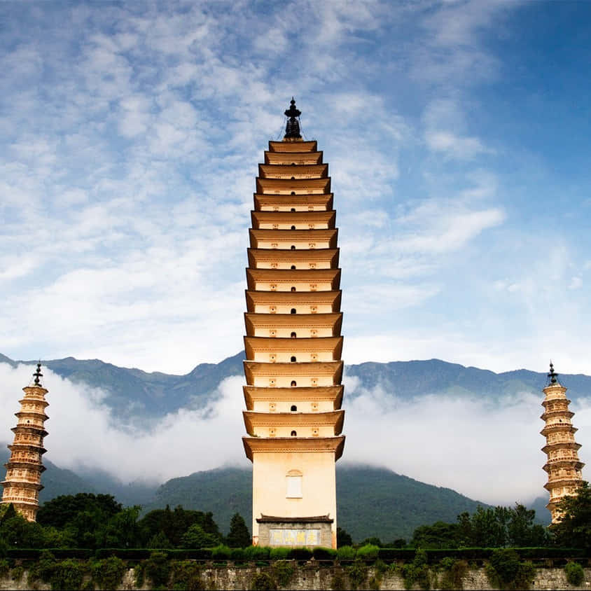 三塔與飄逸雲朵 壁紙 — 三座古塔在藍天白雲和霧氣繚繞的山巒背景下巍峨聳立。
