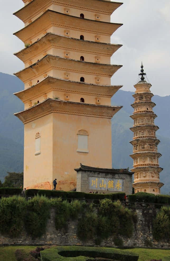 三塔近景照片 壁紙 — 兩座古老的多層寶塔在陰天背景下，聳立在霧氣繚繞的山巒前。