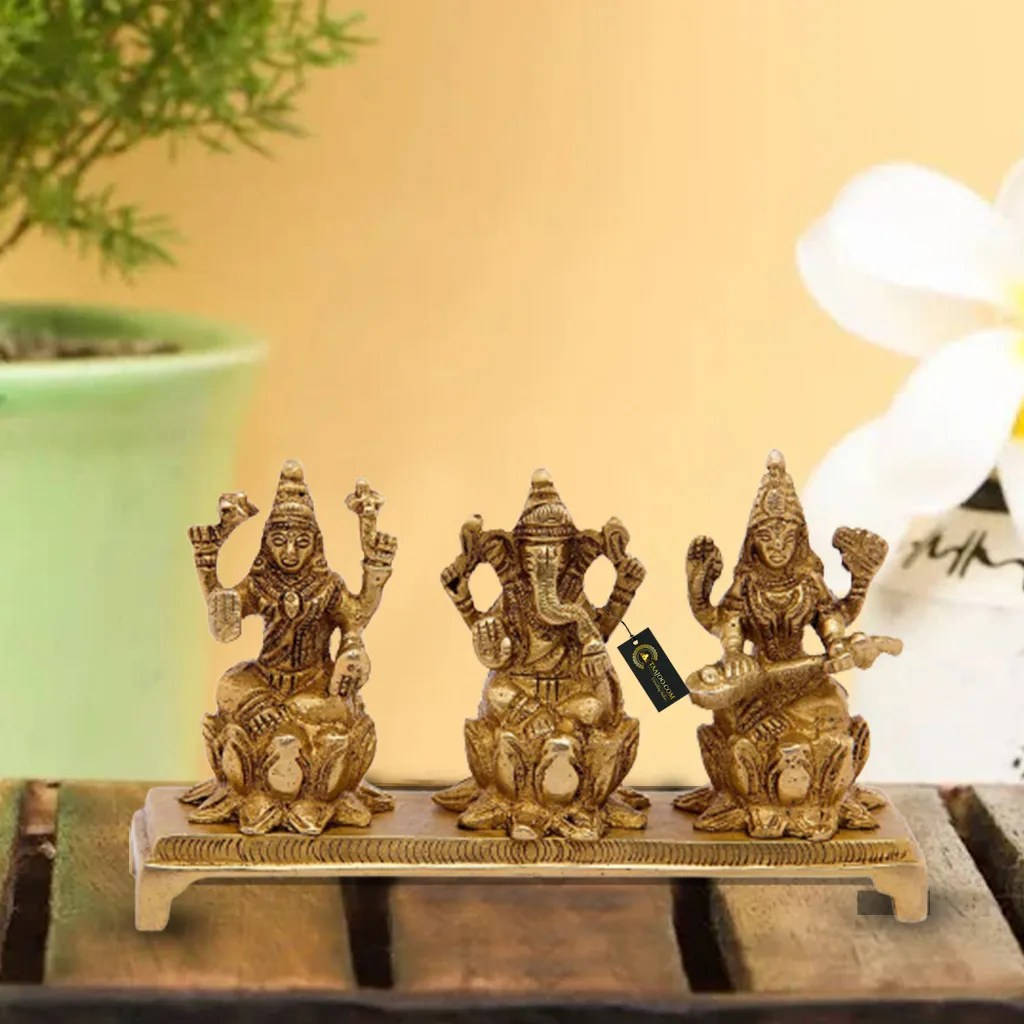 Hindu God 桌布 壁紙 — 三尊金色印度教神像安詳地坐在木架上，旁邊有一盆盆栽和一朵白花。