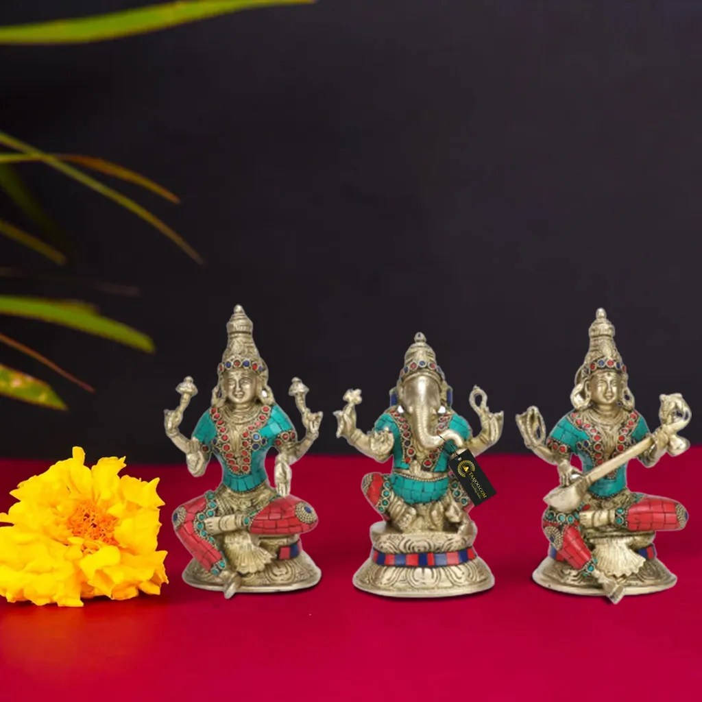 laxmi ganesh saraswati 桌布 壁紙 — 三尊銀色和綠松石色的華麗印度教神像放在紅色表面上，旁邊有一朵鮮黃色的花，背景為深色。