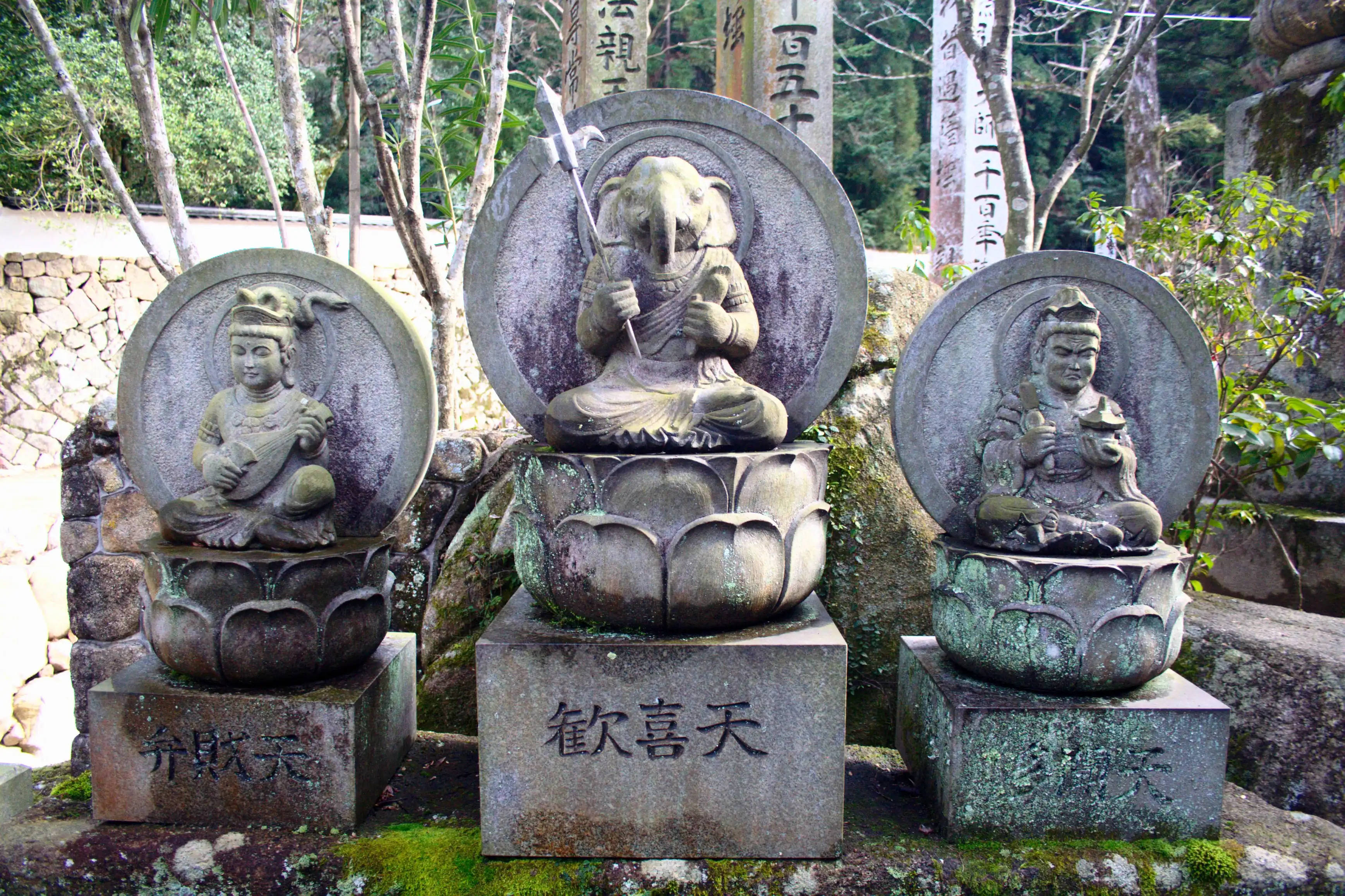 Vishnu 桌布 壁紙 — 三尊風化的佛教神靈石像，安詳地坐在蓮花座上，周圍是長滿青苔的岩石和樹木，位於寧靜的寺院花園中。