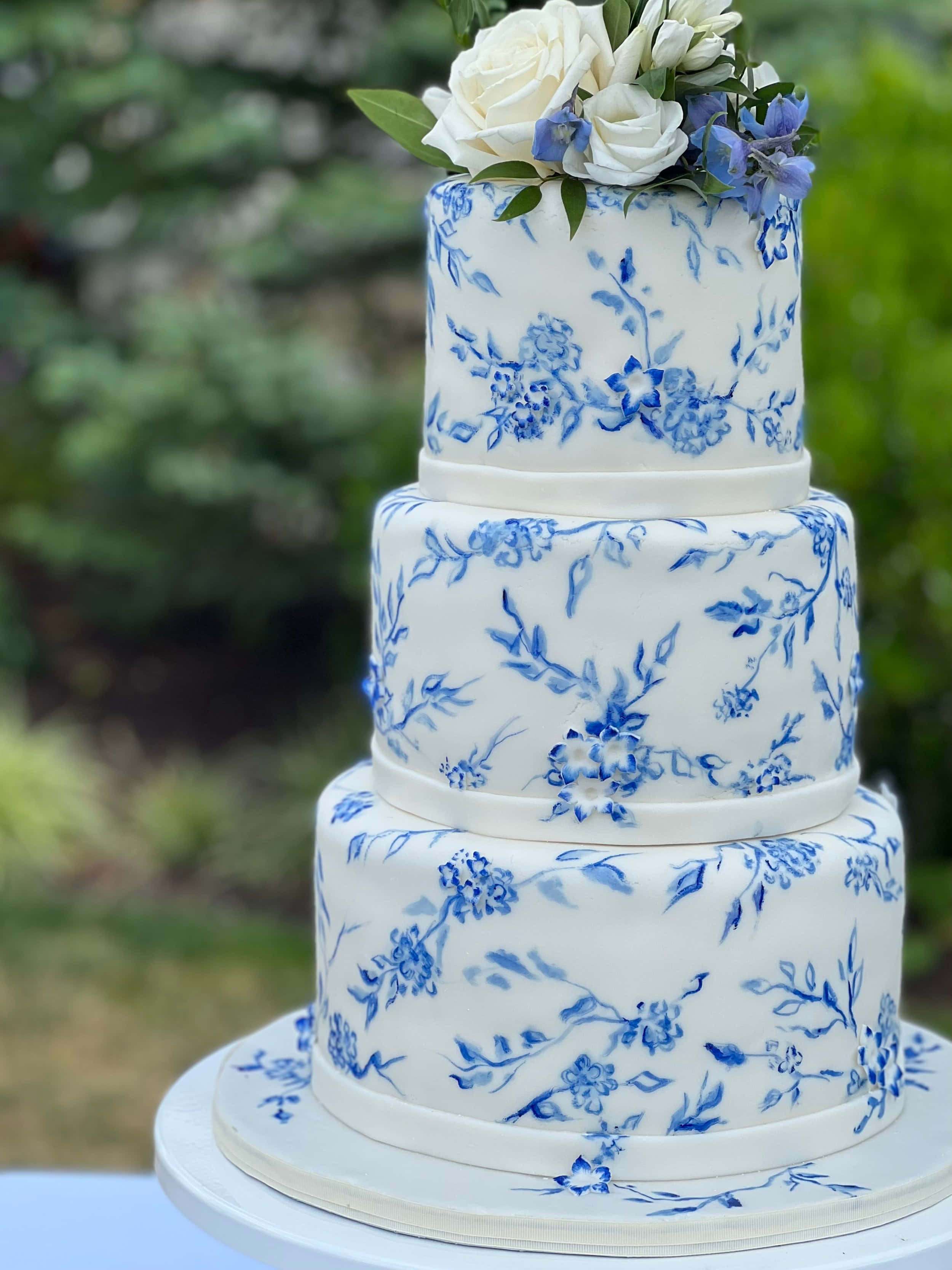Cake Fondant 桌布 壁紙 — 三層白色結婚蛋糕，飾以精緻的藍色花卉圖案，頂部綴有白色和藍色花朵。