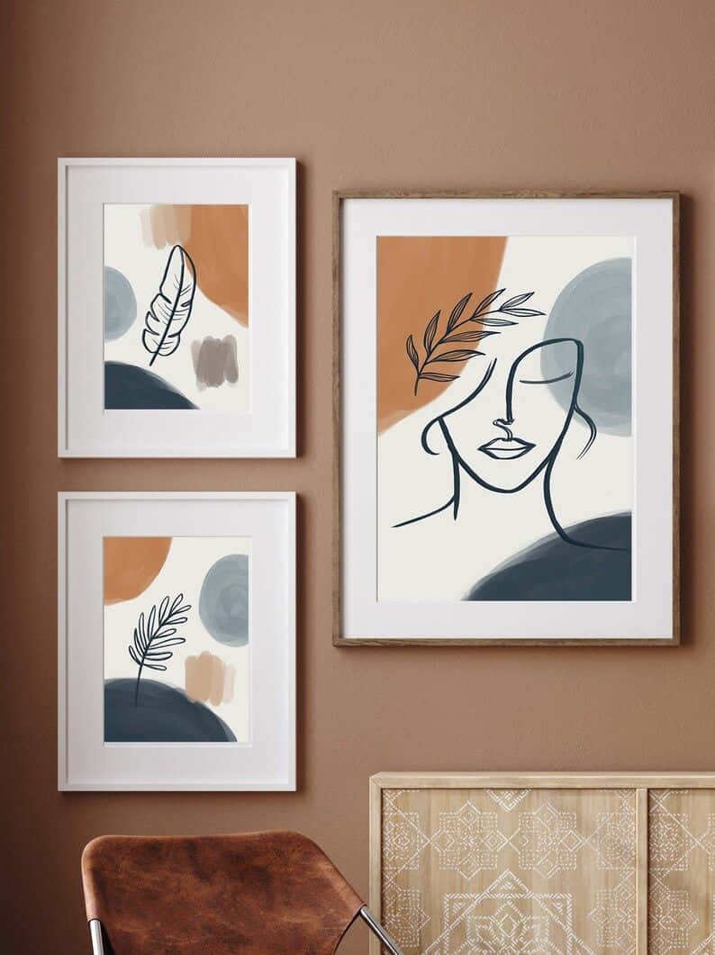Minimalist Painting 桌布 壁紙 — 三幅帶有葉子和面孔極簡線條畫的框裝抽象藝術品，掛在溫暖的棕色牆上，下方是圖案櫃和皮革椅。