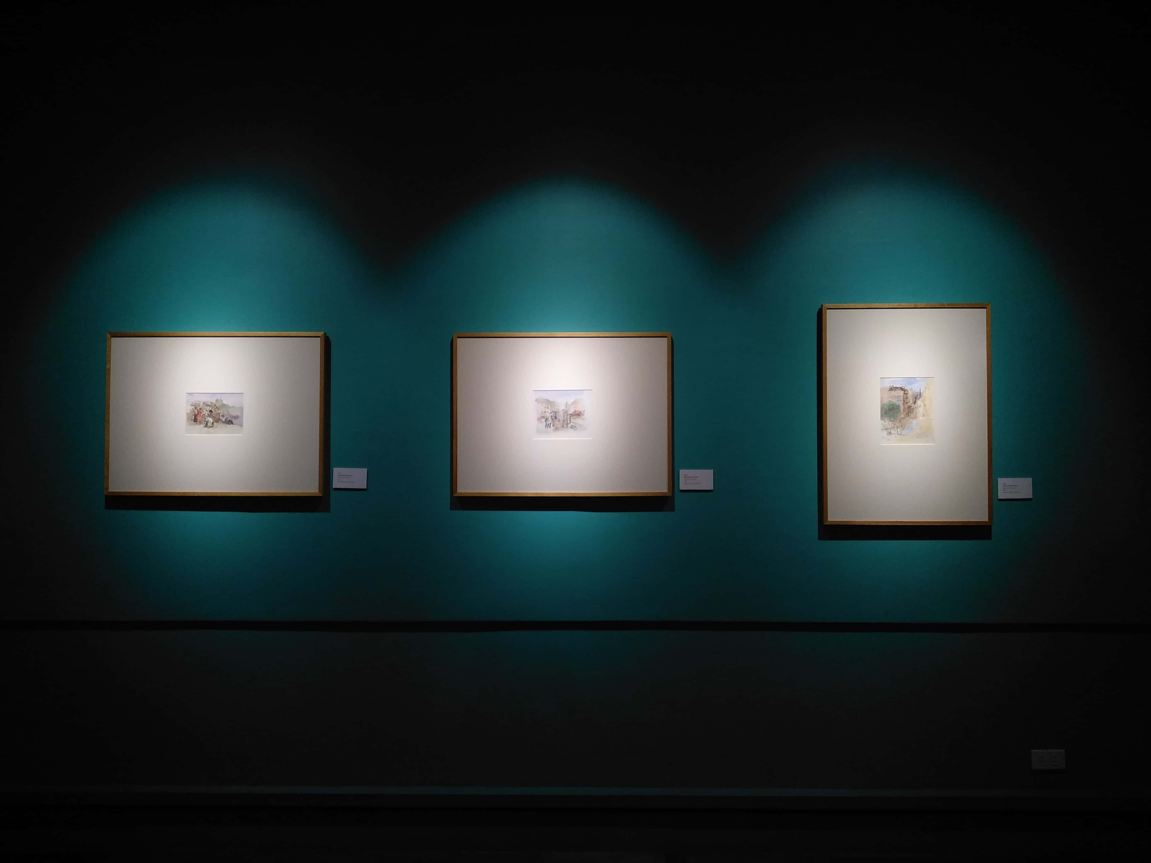 Gallery 桌布 壁紙 — 三幅裱框藝術品在昏暗環境光線下，於聚光燈下在深青色畫廊牆壁上發光。