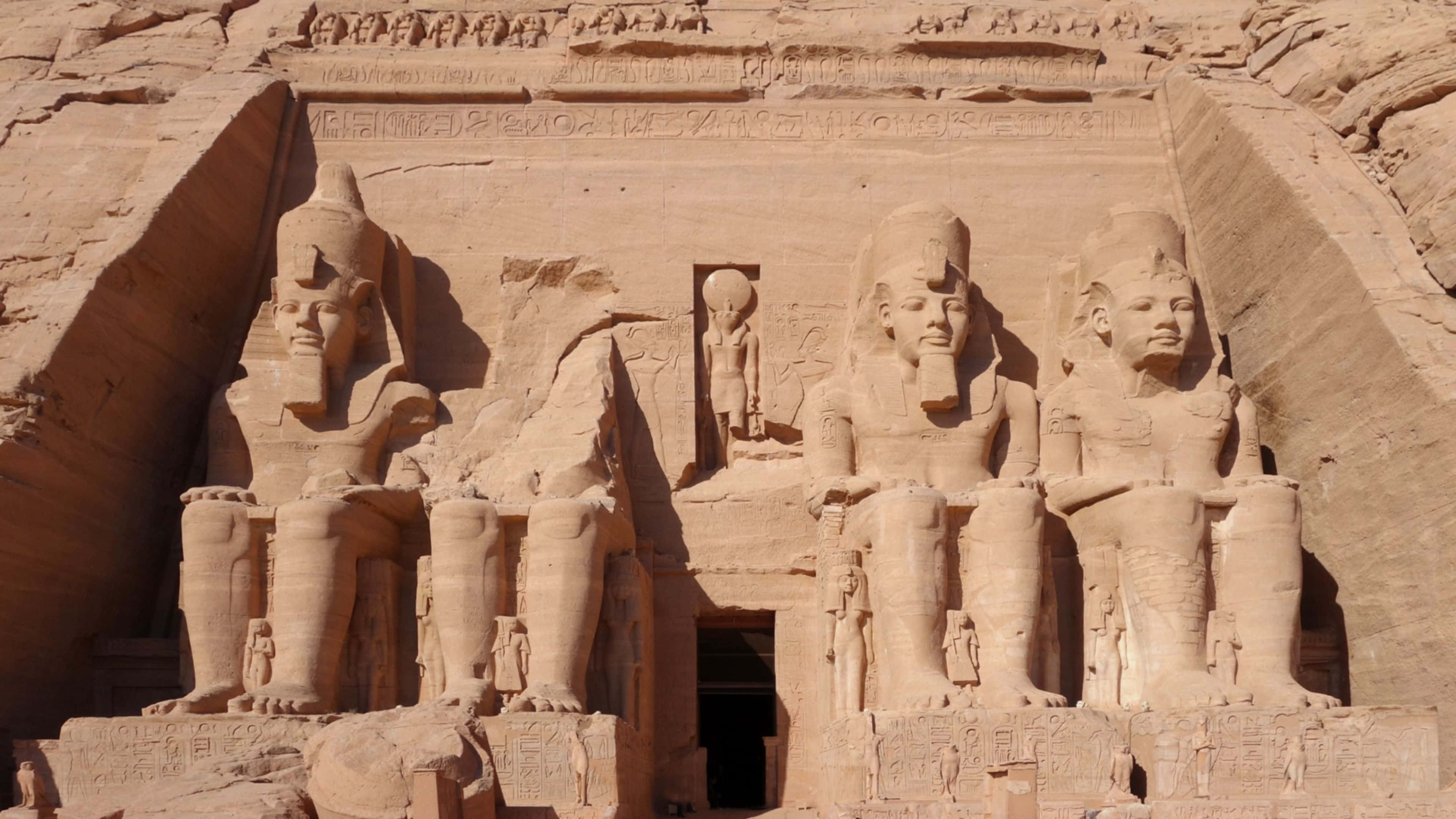 Ancient Egypt 桌布 壁紙 — 三座巨大嘅坐姿法老雕像雕刻喺砂岩懸崖面上，上面有象形文字。