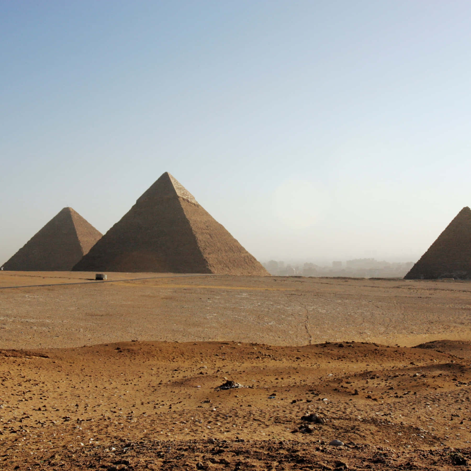 Ancient Egypt 桌布 壁紙 — 三座巨大的古老金字塔從廣闊的沙漠中升起，在清澈的藍天下，前景中有一輛孤獨的車輛。