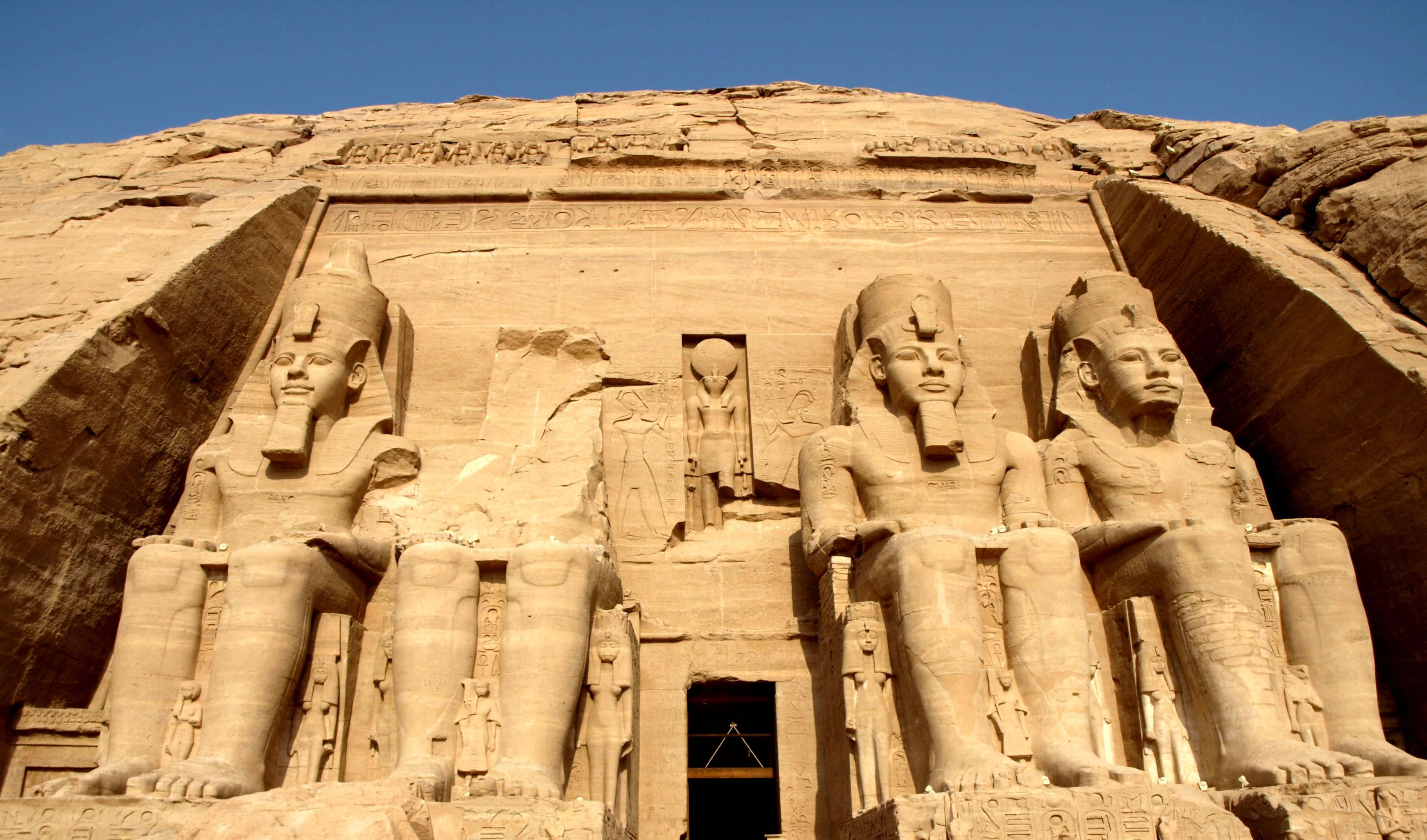 Egypt 桌布 壁紙 — 三座巨大的坐姿法老雕像，雕刻在砂岩懸崖上，背景是晴朗的藍天。