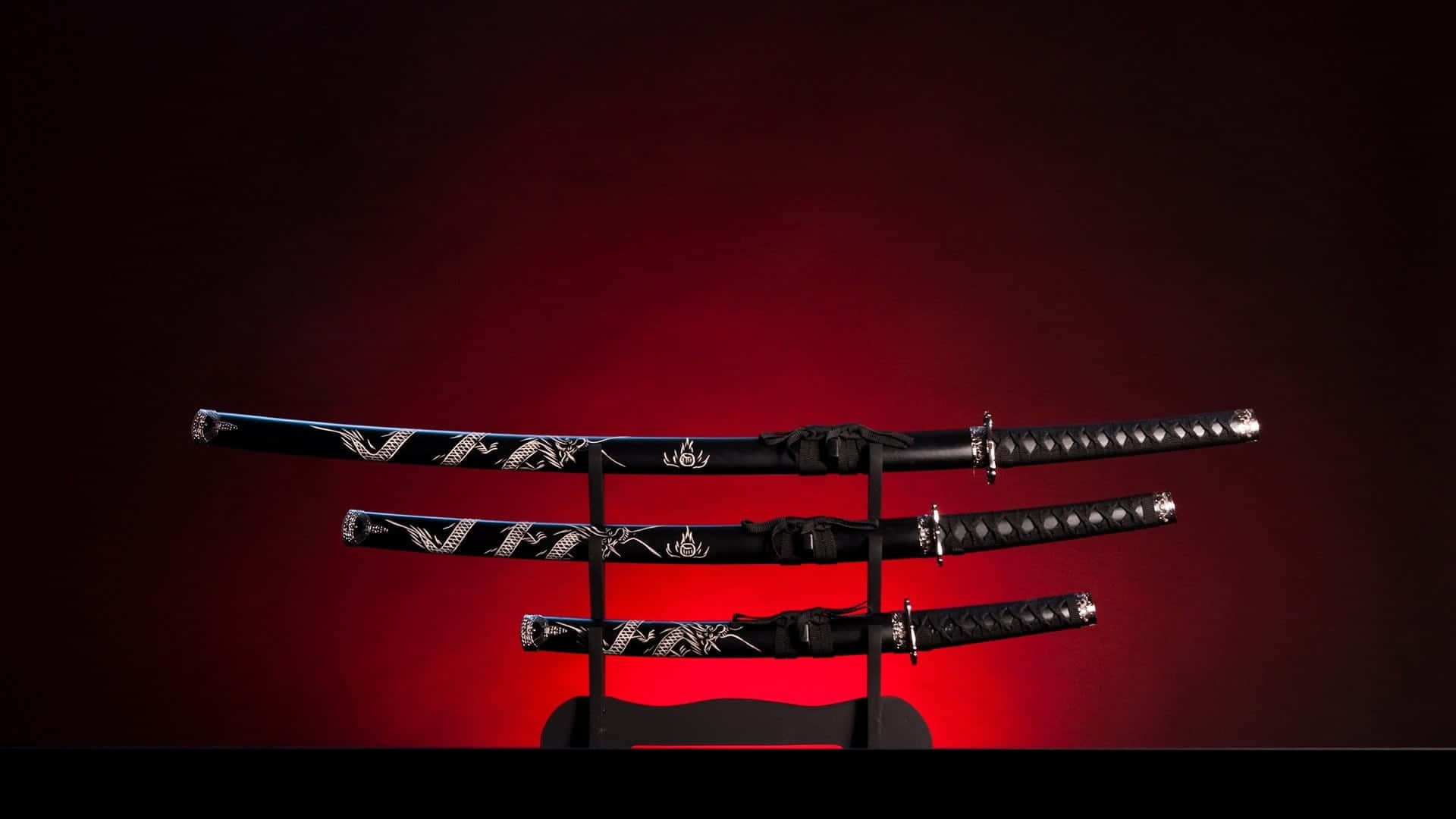 Samurai Sword 桌布 壁紙 — 三把裝飾華麗的黑色日本刀，帶有銀色龍紋圖案，放置在漸變紅色背景前的支架上。