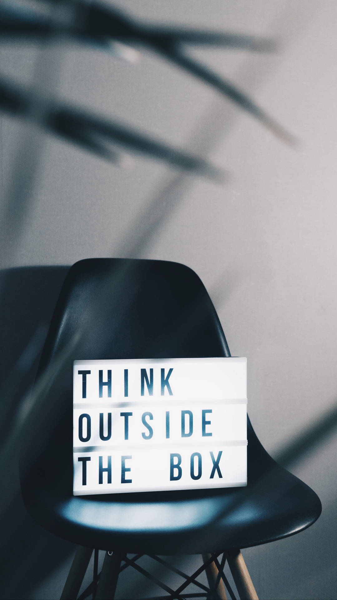 黑色椅子上的燈箱寫著 think outside the box，在牆上投射陰影