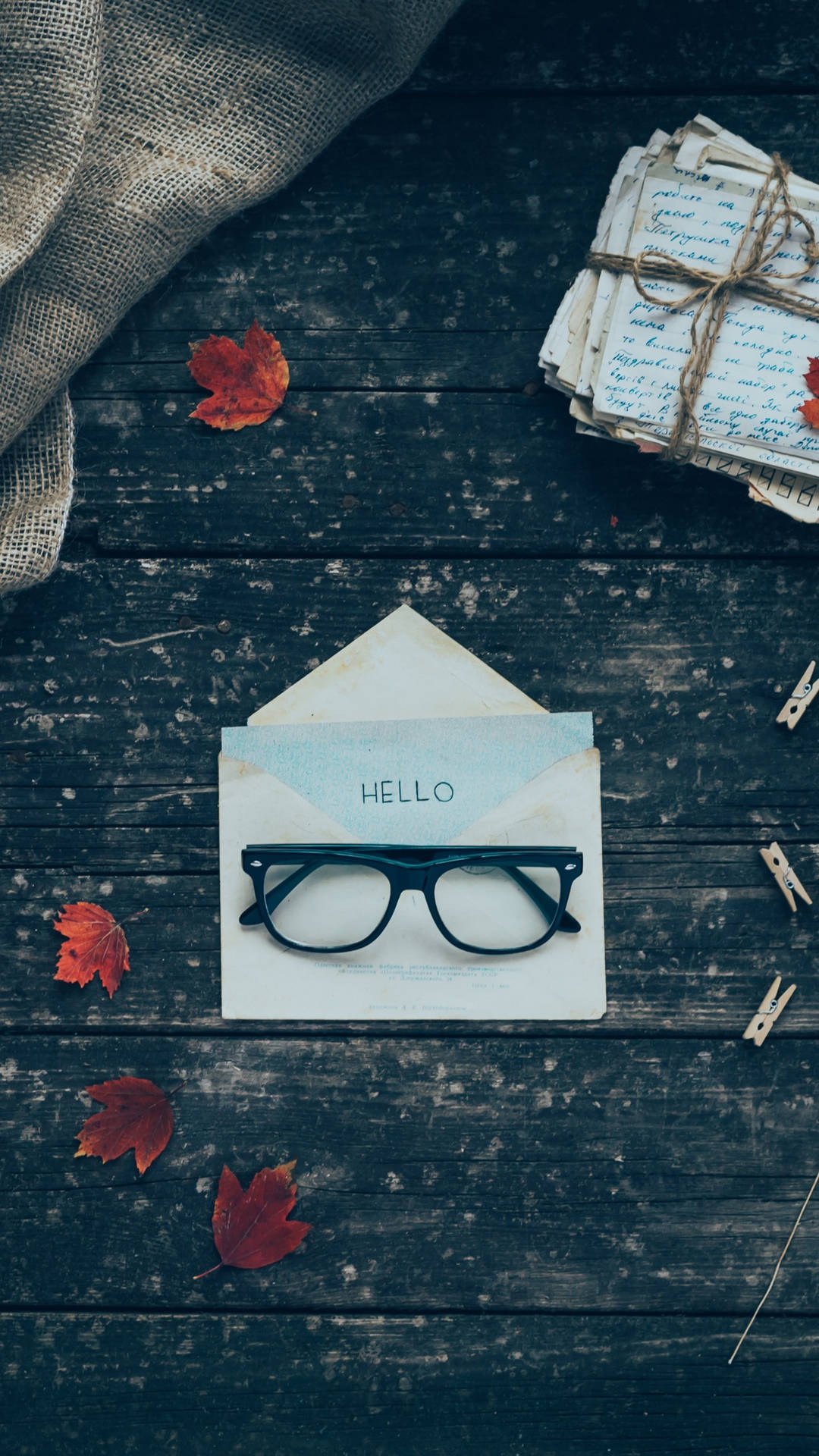 眼鏡在寫有'hello'的信封上，周圍是秋葉和綁著的信件在木頭上。