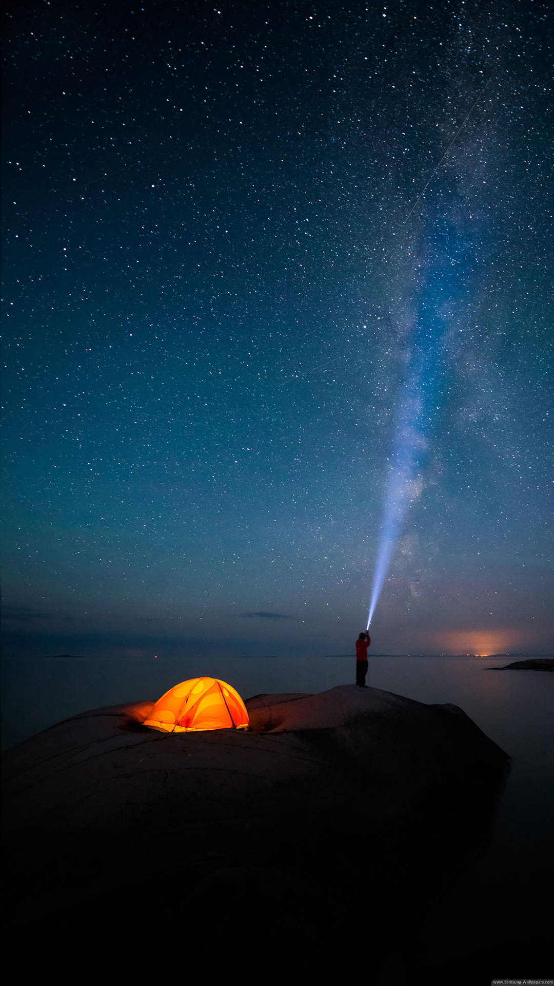 夜晚在懸崖上露營的人，發光的帳篷和指向銀河的手電筒。