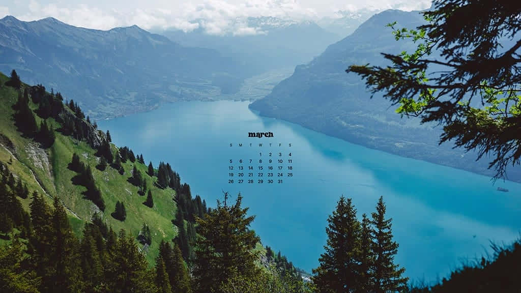 March Desktop 桌布 壁紙 — 三月寧靜的山湖日曆，周圍環繞著茂密的綠色松樹，天空部分多雲。