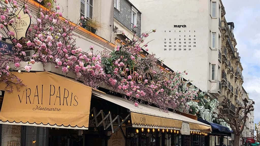 March Desktop 桌布 壁紙 — 三月巴黎街角，粉紅花朵與咖啡館遮陽篷點綴，天空部分多雲。
