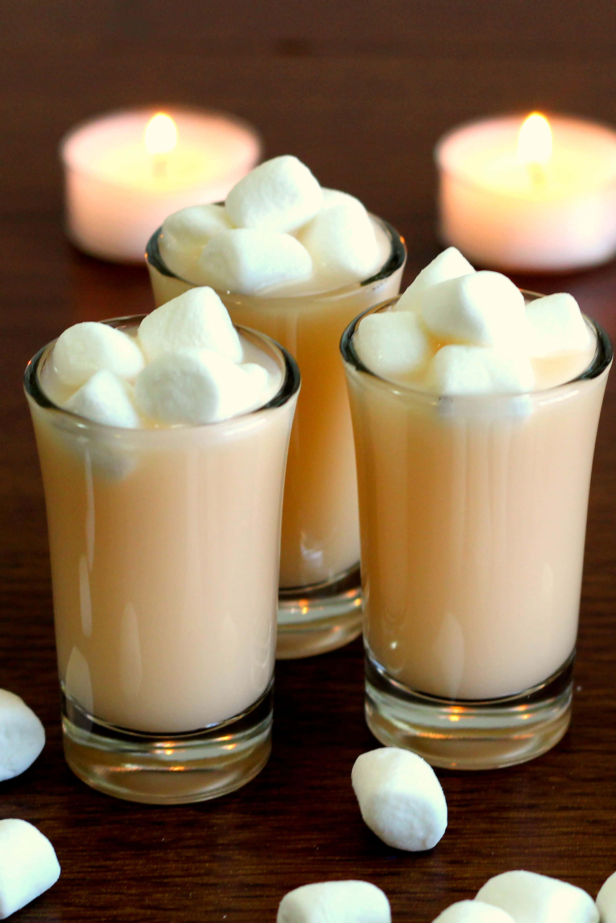Winter Drinks 桌布 壁紙 — 三杯 creamy 熱可可，上面有 fluffy 棉花糖，放在木桌上，旁邊有發光嘅茶燭。