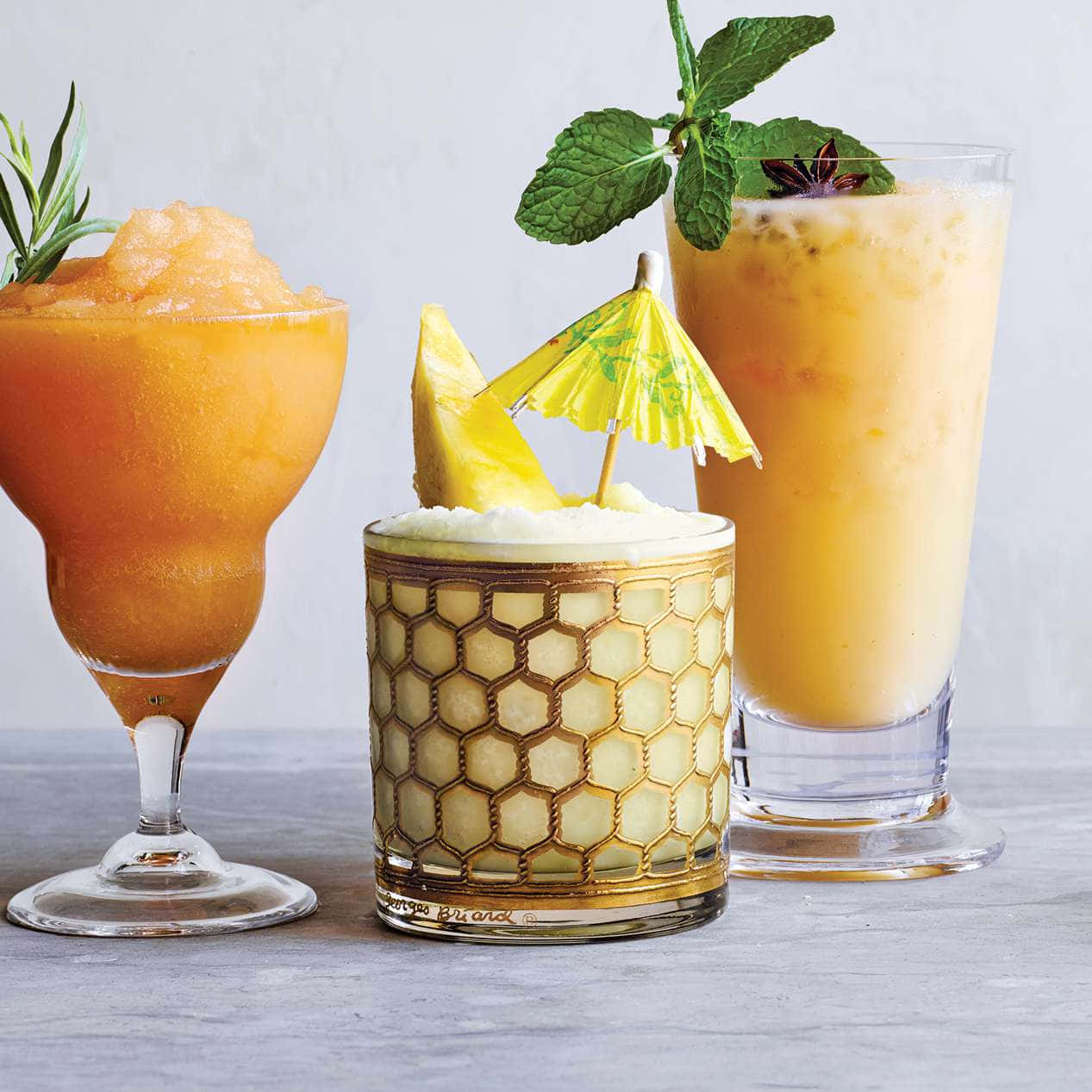 Beautiful Drink 桌布 壁紙 — 三杯充滿活力的熱帶雞尾酒，飾以薄荷、菠蘿和迷迭香，放在灰色表面上。