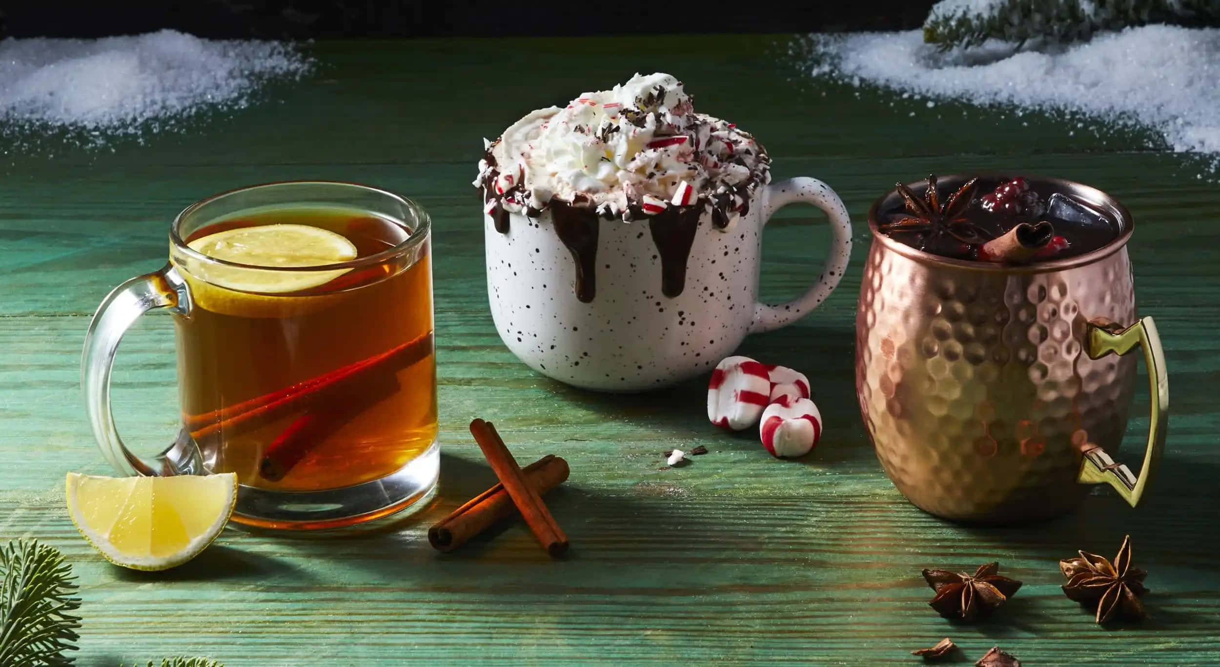 Winter Drinks 桌布 壁紙 — 三杯節日冬季飲品，配上忌廉、糖果手杖和香料，放在一個白雪覆蓋的綠色木桌上。