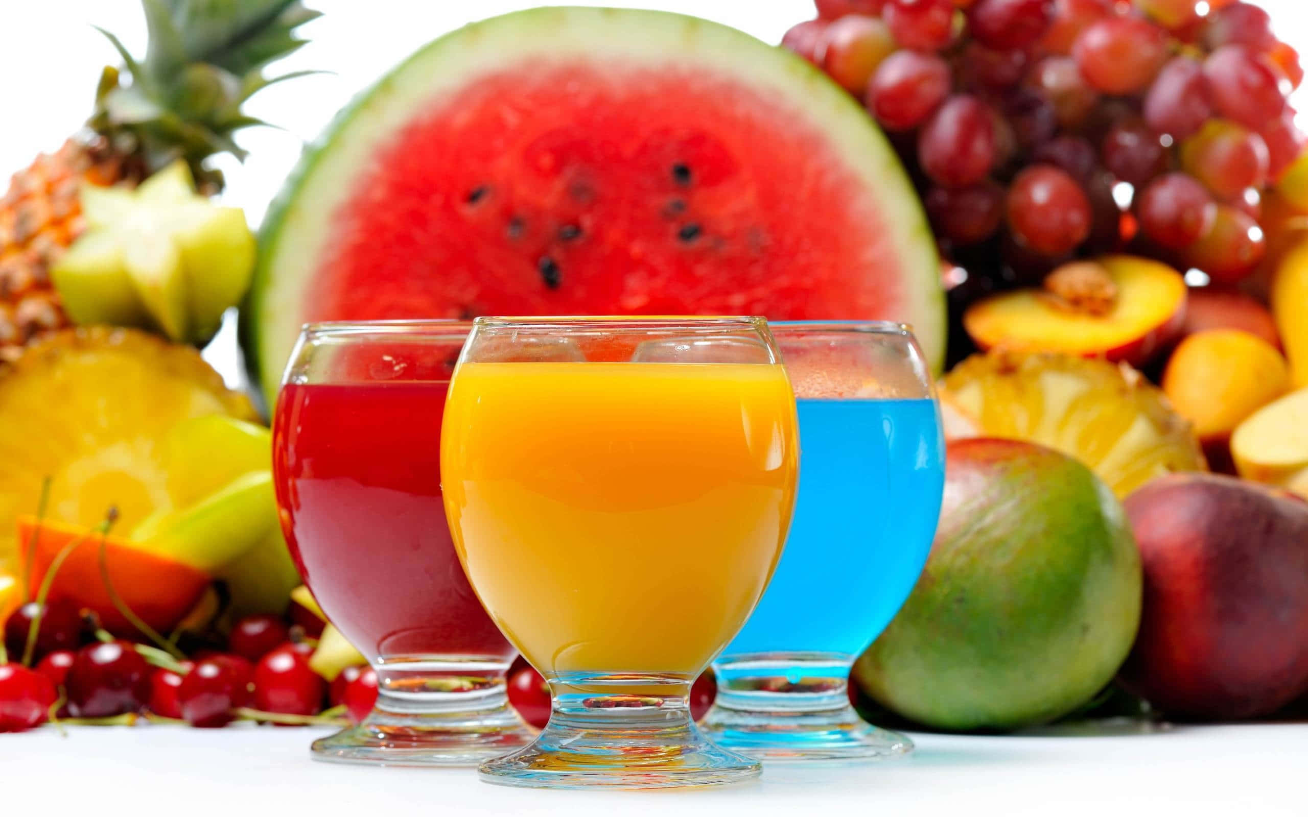 Food And Beverage 桌布 壁紙 — 三杯色彩繽紛的果汁放在白色表面上，周圍環繞著豐富多樣的新鮮熱帶水果。