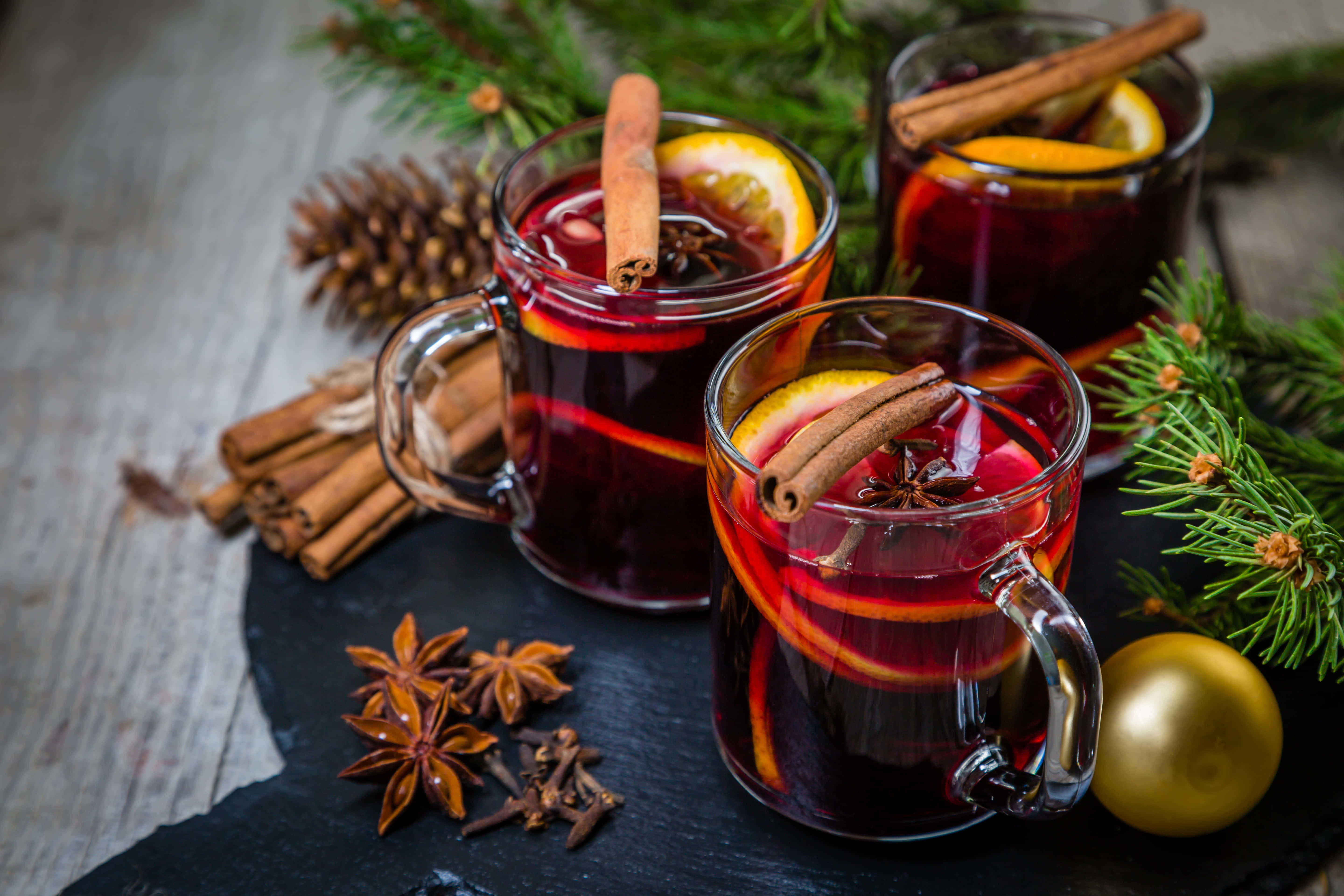 Mulled Wine 桌布 壁紙 — 三杯香料熱紅酒，飾以肉桂棒和橙片，放在深色石板板上，旁邊有松枝、松果、八角星和金色裝飾品。