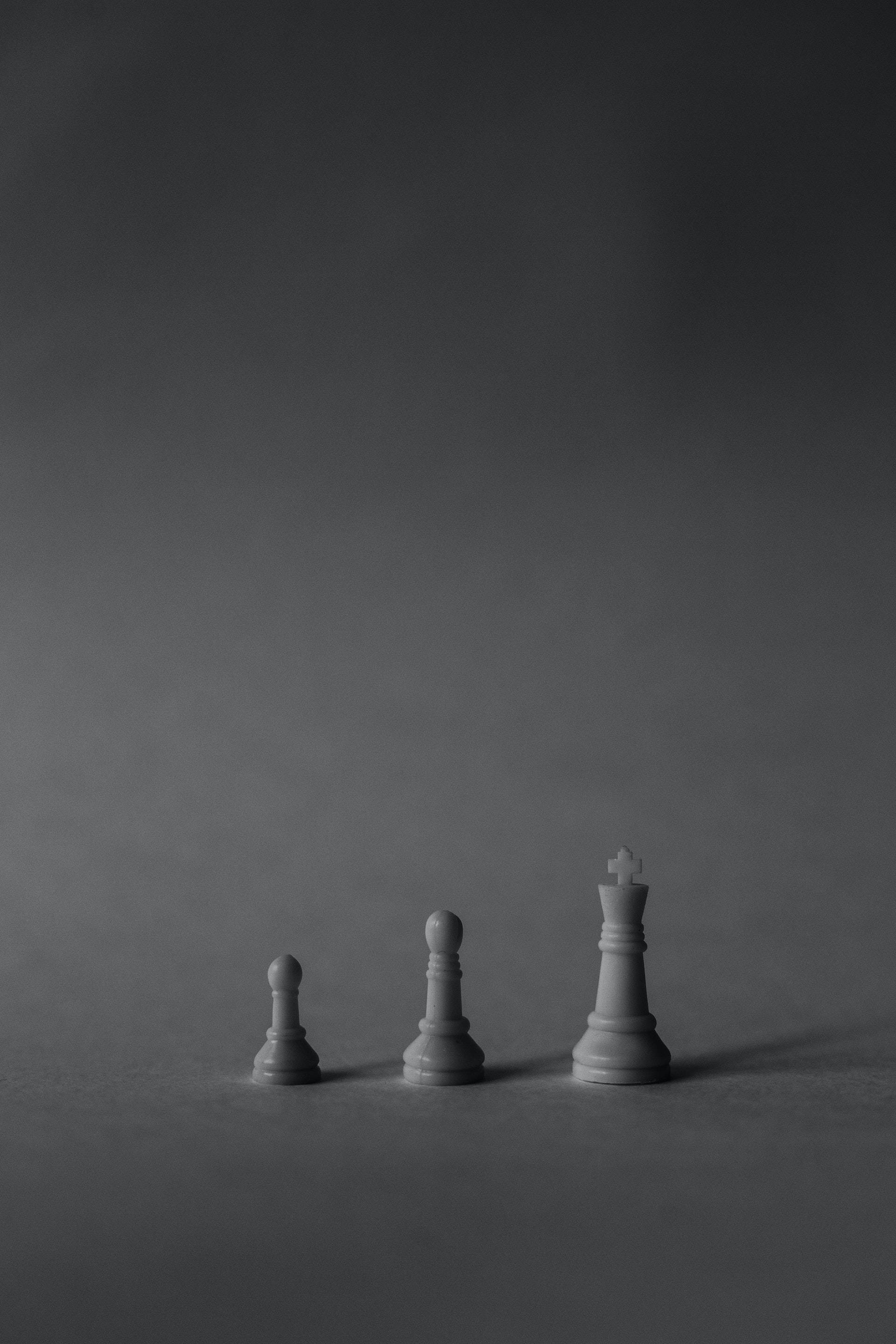 灰色 桌布 壁紙 — 三枚極簡風格的國際象棋棋子，在柔和的灰色漸變背景上以遞增尺寸升起。