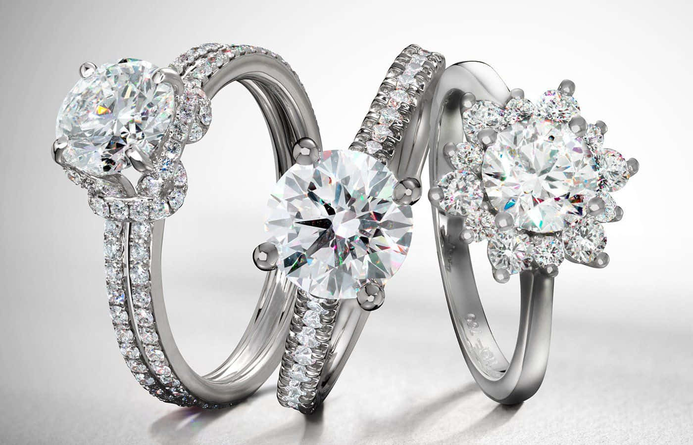 Jewelry Design 桌布 壁紙 — 三枚璀璨奪目的鑽石訂婚戒指，鑲工精緻，在柔和的工作室燈光下，於極簡白色背景上閃耀光芒。