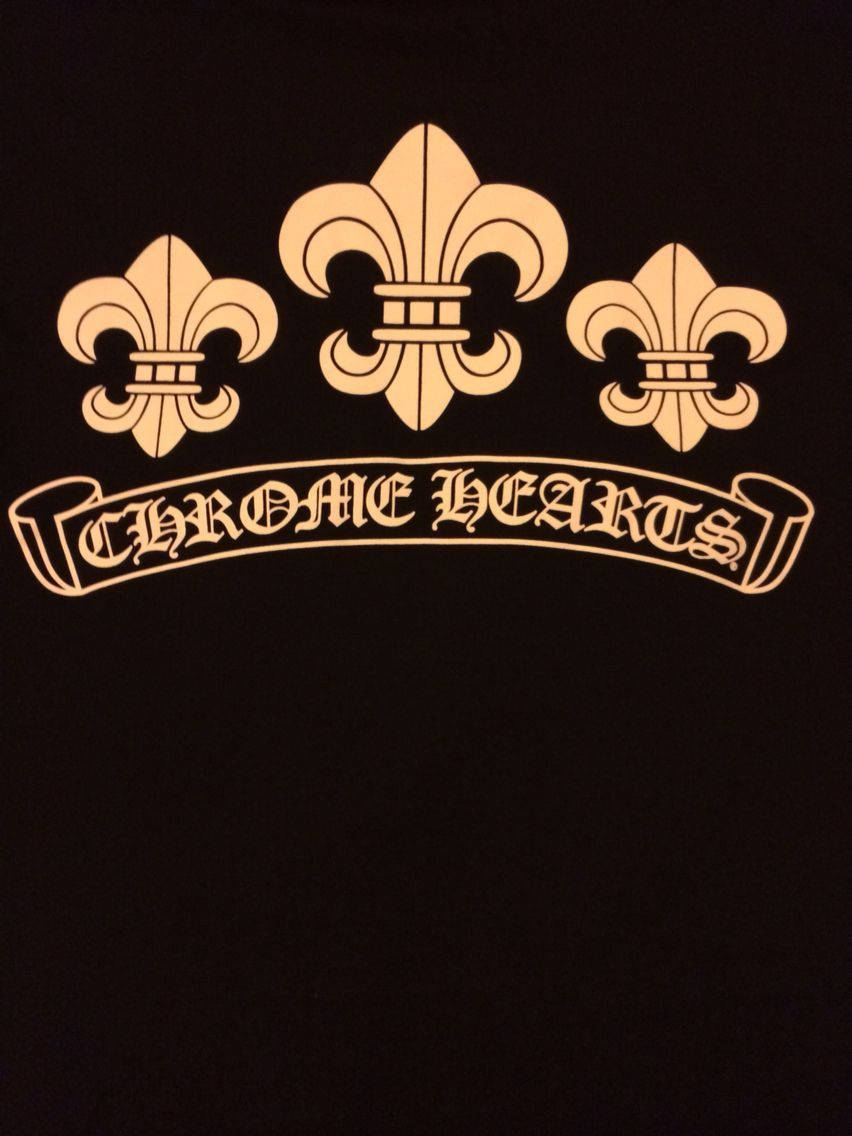 三枚金色 Chrome Hearts 象徵圖案 壁紙 — 一件黑色T恤展示金色Chromatic Hearts標誌，上方有三朵鳶尾花，下方有橫幅。