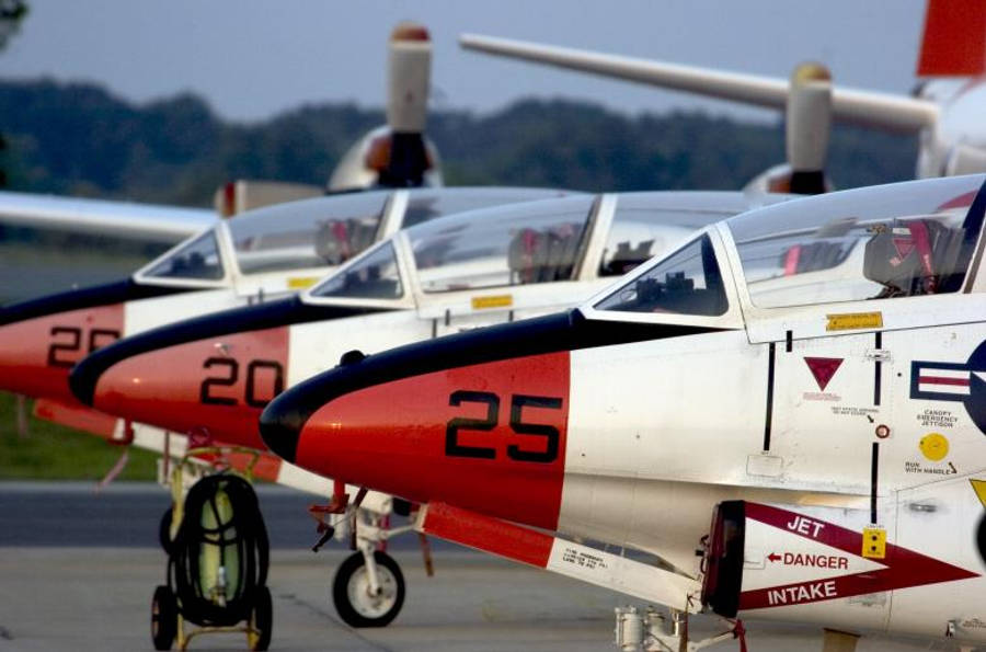 三架美國海軍戰鬥機整齊停放 壁紙 — 一排紅白相間的軍用教練機，帶有可見的駕駛艙罩和編號機身，停放在機場停機坪上。