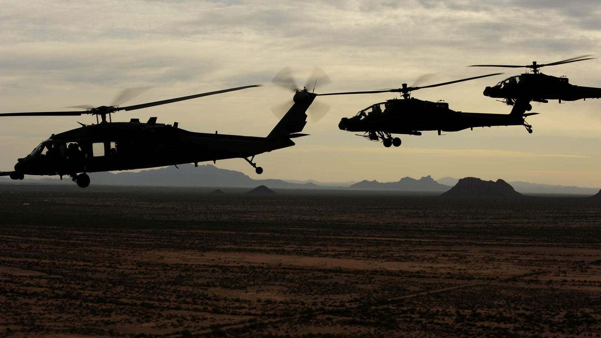 Helicopter 桌布 壁紙 — 三架軍用直升機以剪影形式編隊飛行，背景是昏暗的沙漠天空和遠山。