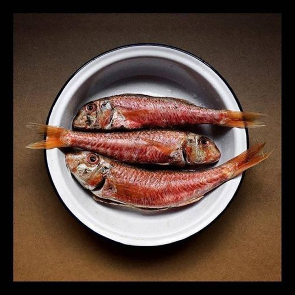 三條乾紅魚在一個白色琺瑯碗裡，放在棕色表面上。