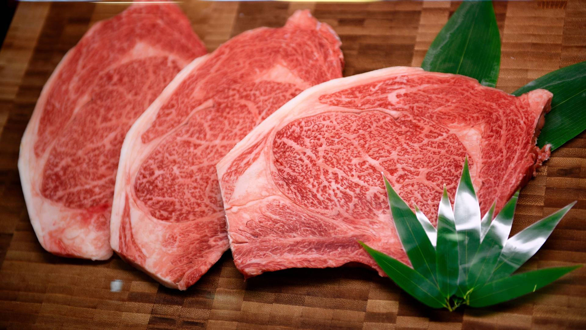 三塊高品質大理石紋牛肉扒放在木砧板上，配以竹葉。