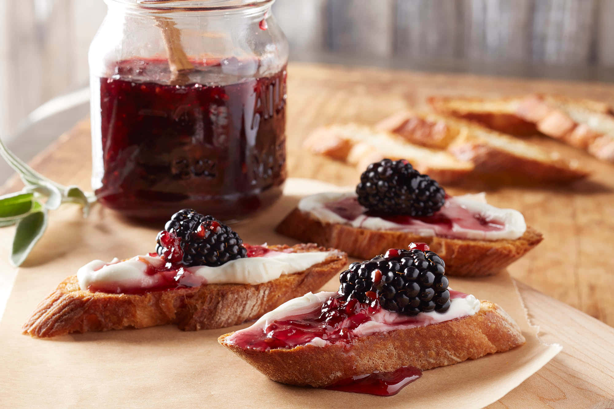 Blackberry Jam 桌布 壁紙 — 三片多士麵包，上面塗有 creamy 白色醬料和新鮮黑莓，淋上光澤深紅色果醬，旁邊放著一個玻璃罐在木板上。