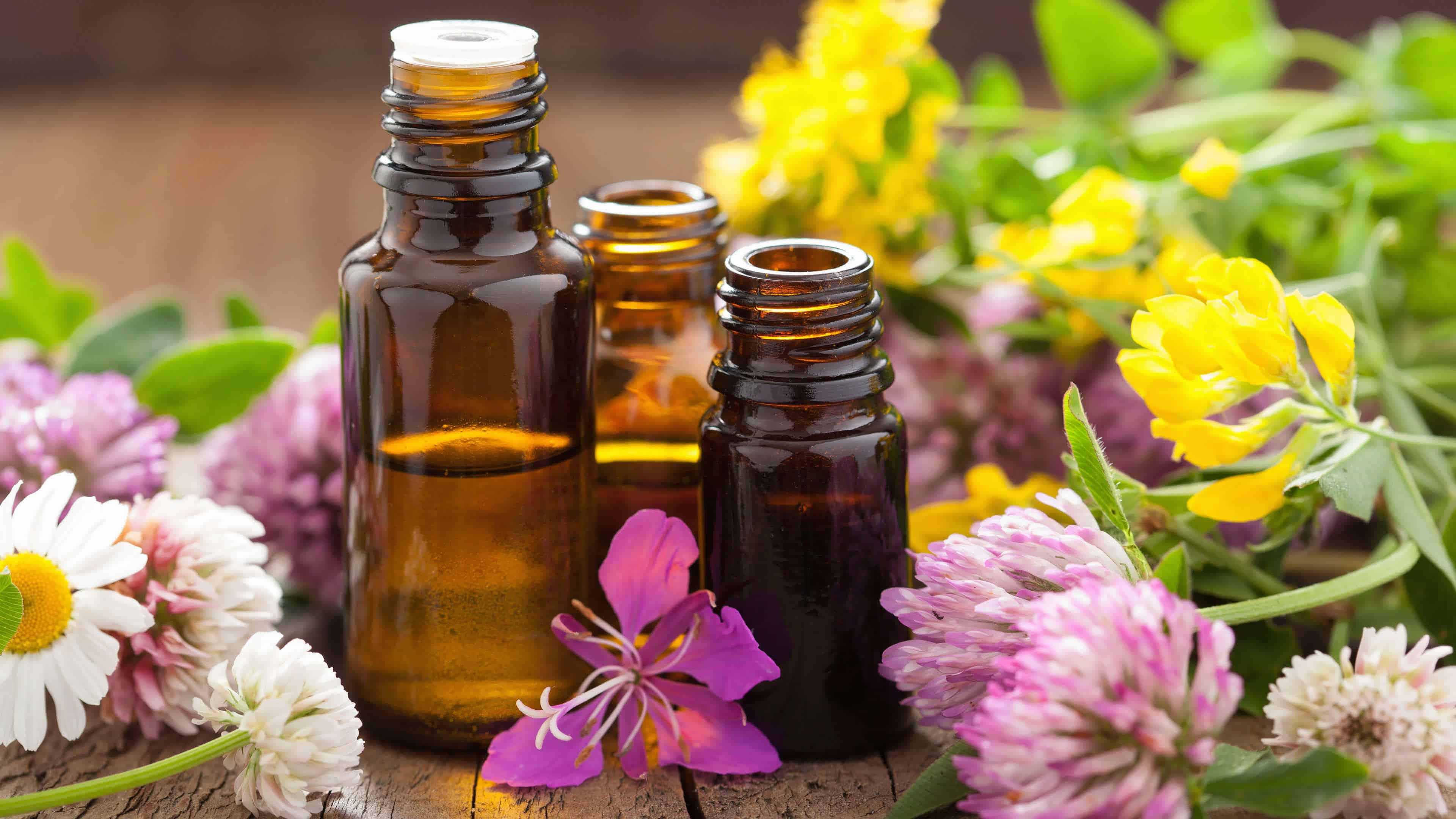 Essential Oil 桌布 壁紙 — 三瓶琥珀色玻璃精油瓶， nestled 在充滿活力的黃色、粉紅色和白色野花中，放在質樸的木質表面上。