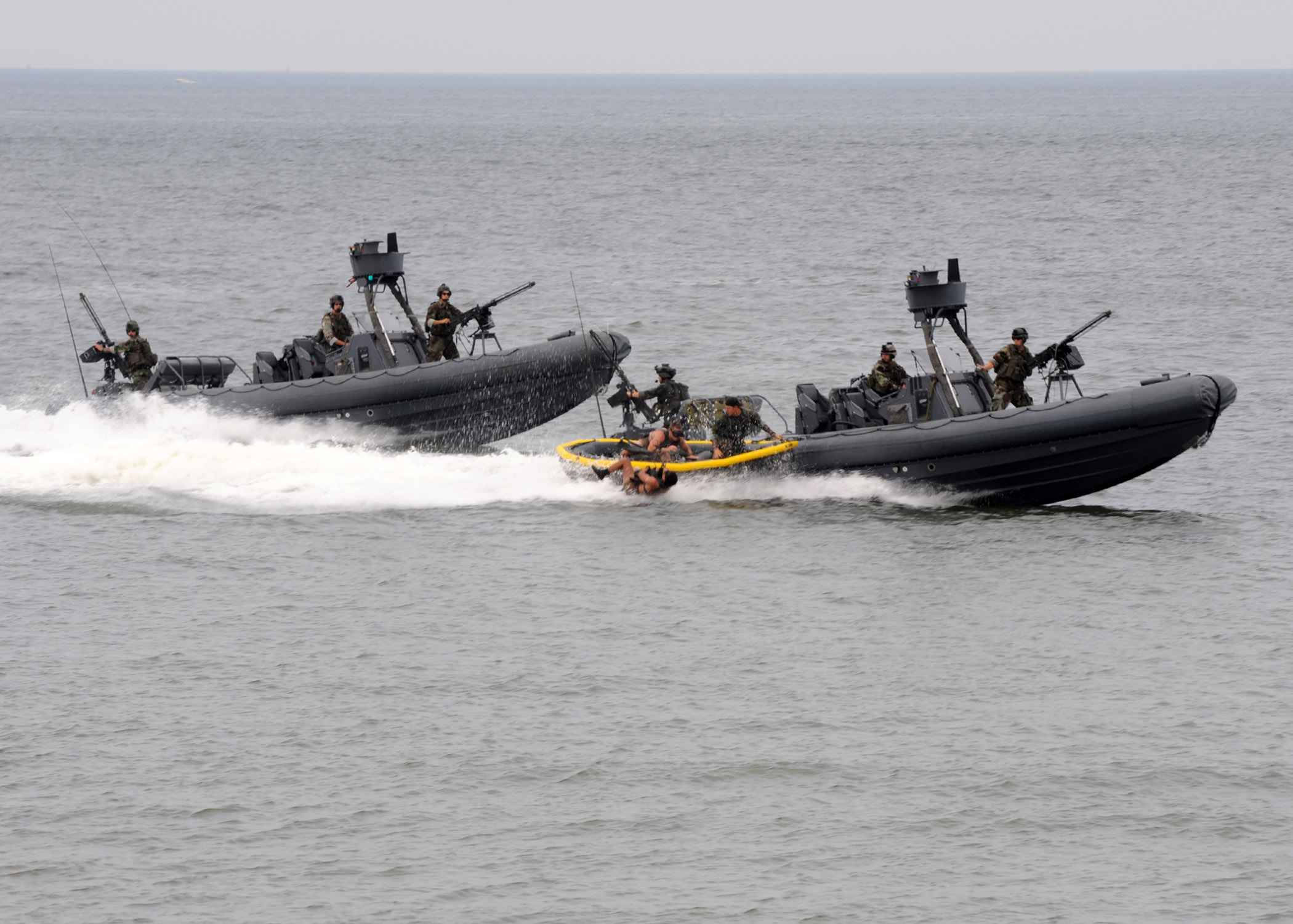 三艘美國海軍快艇執行任務 壁紙 — 兩艘黑色軍用快艇載著武裝士兵在灰色海面上飛馳，激起白色浪花。