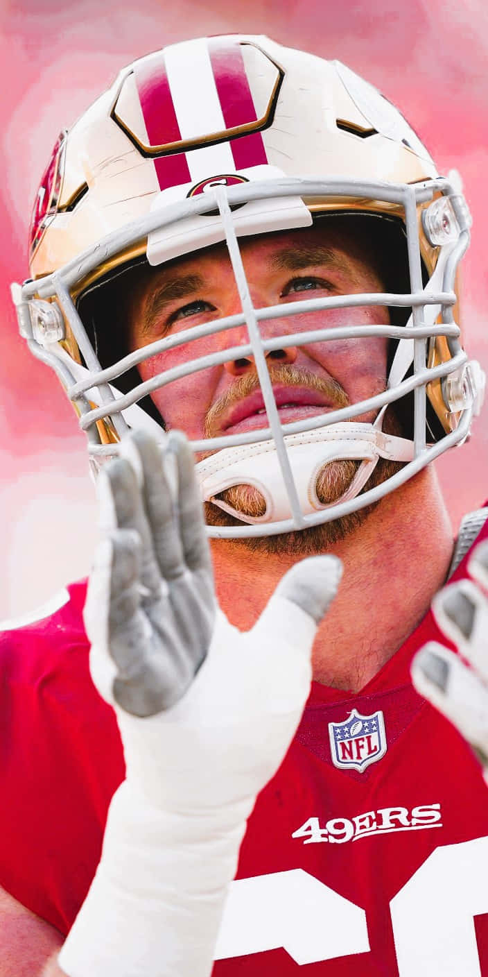 Mike Mcglinchey 桌布 壁紙 — 三藩市49人美式足球員身穿紅色球衣及頭盔，在柔和粉紅色背景前向球迷揮手的特寫。