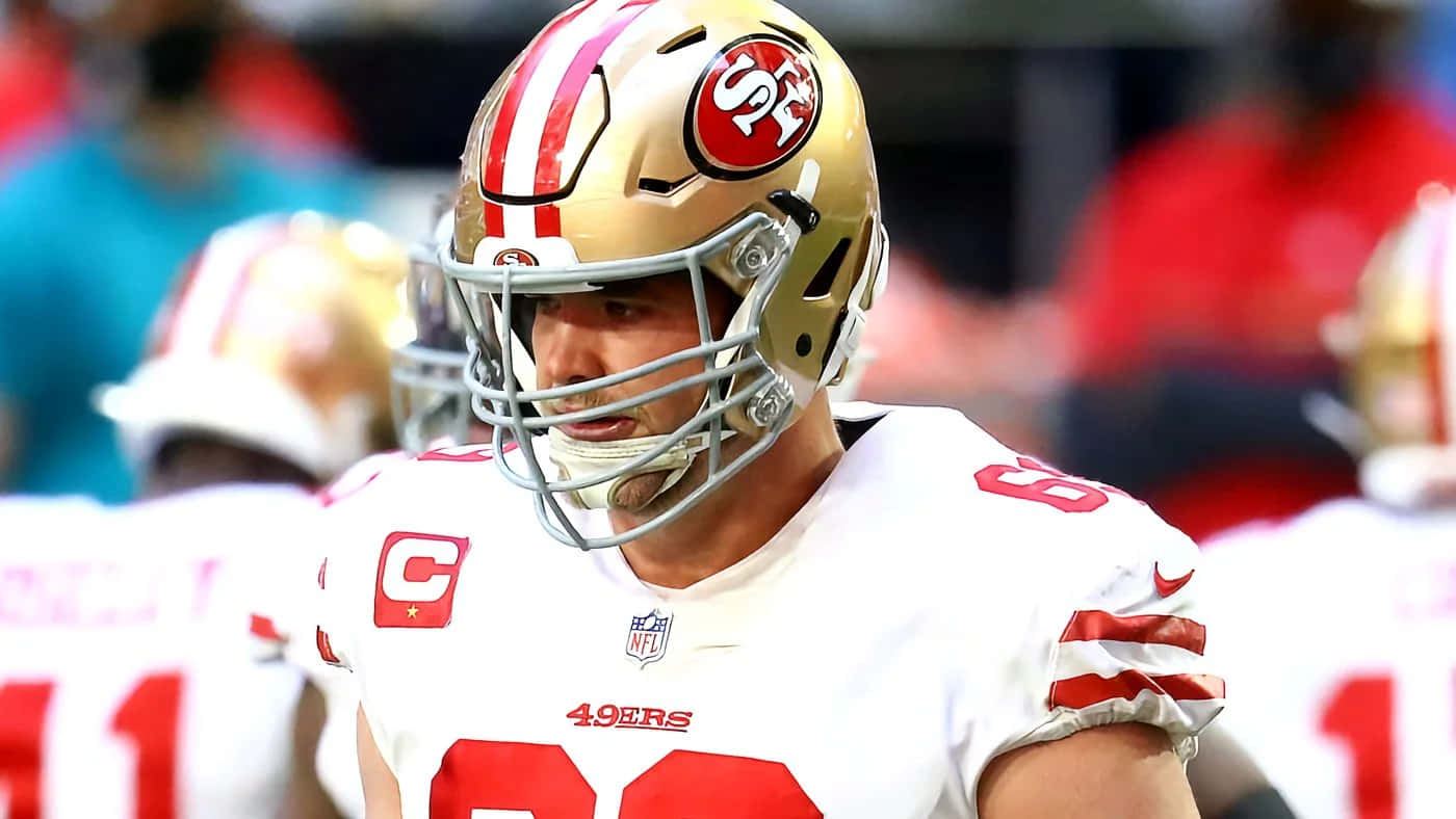 Mike Mcglinchey 桌布 壁紙 — 三藩市四九人美式足球員近距離特寫，戴著金色頭盔，身穿帶有紅色點綴的白色球衣，在球場上。