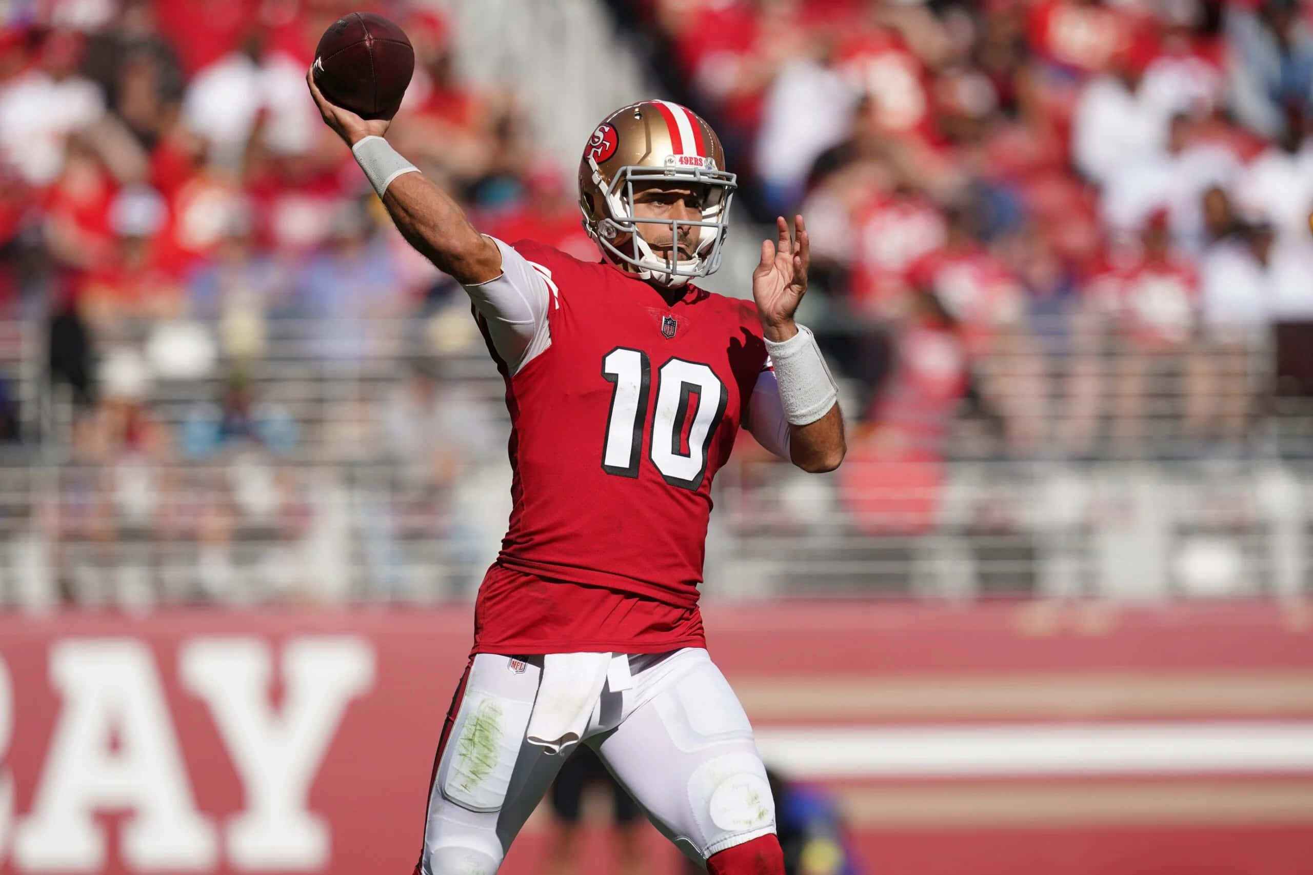 Jimmy Garoppolo 桌布 壁紙 — 三藩市四九人隊的四分衛身穿紅色10號球衣，在日間比賽中擲出橄欖球，背景是模糊的球場觀眾。