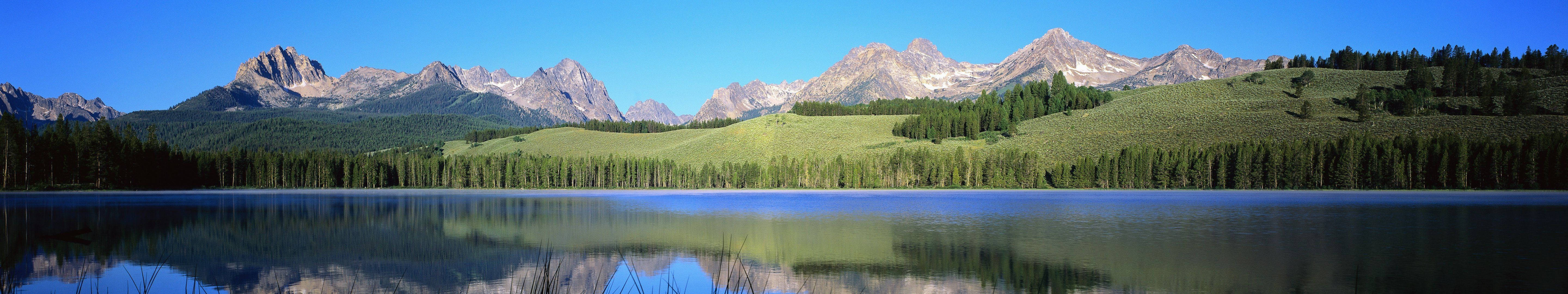 寧靜的山湖映照著雪峰和綠色森林，在清澈的藍天下。