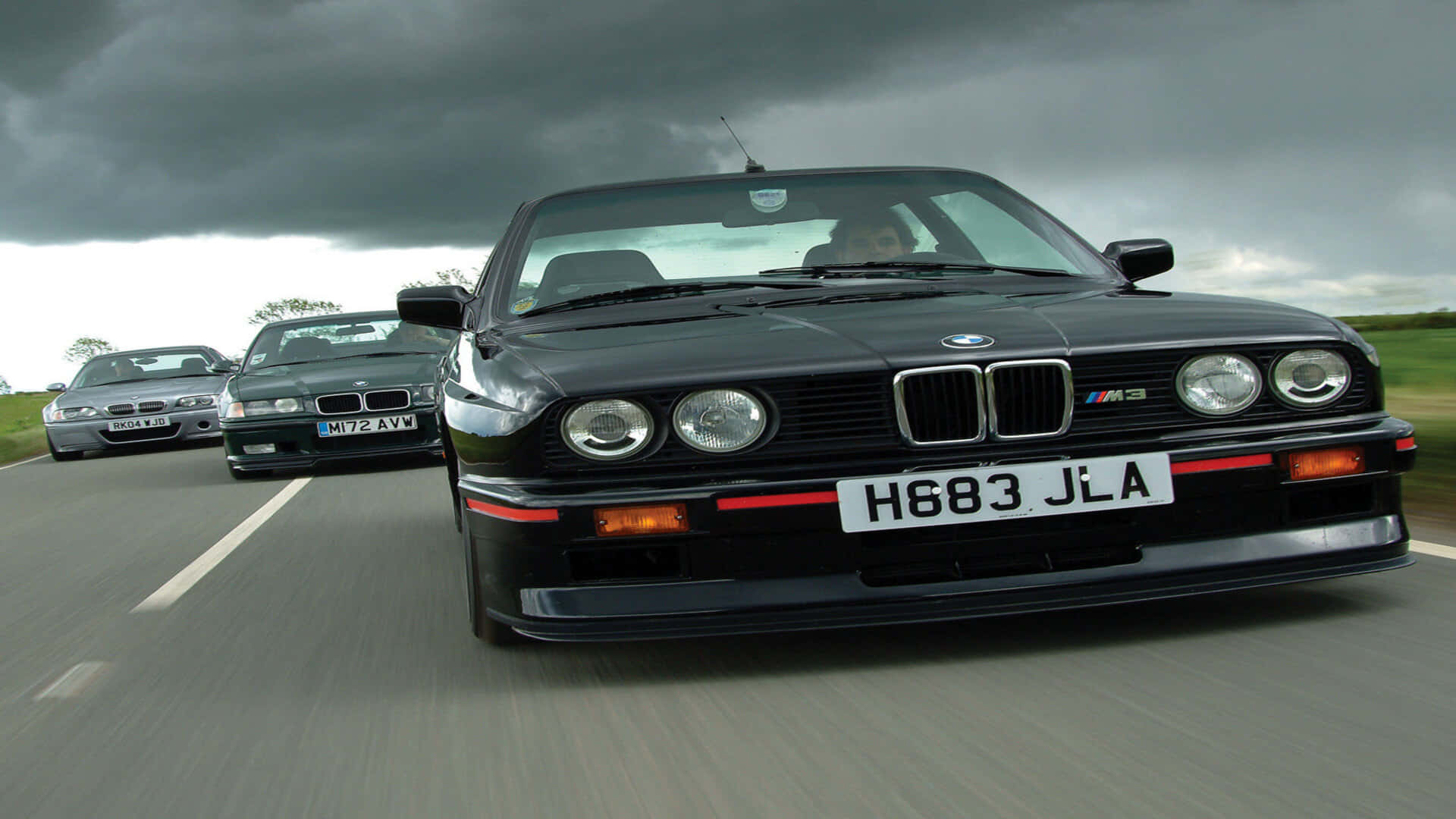 三輛BMW M3汽車 1920x1080 M系列背景 壁紙 — 三輛黑色BMW M3在暴風雨的天空下，以模糊的動態在濕滑的道路上競速。