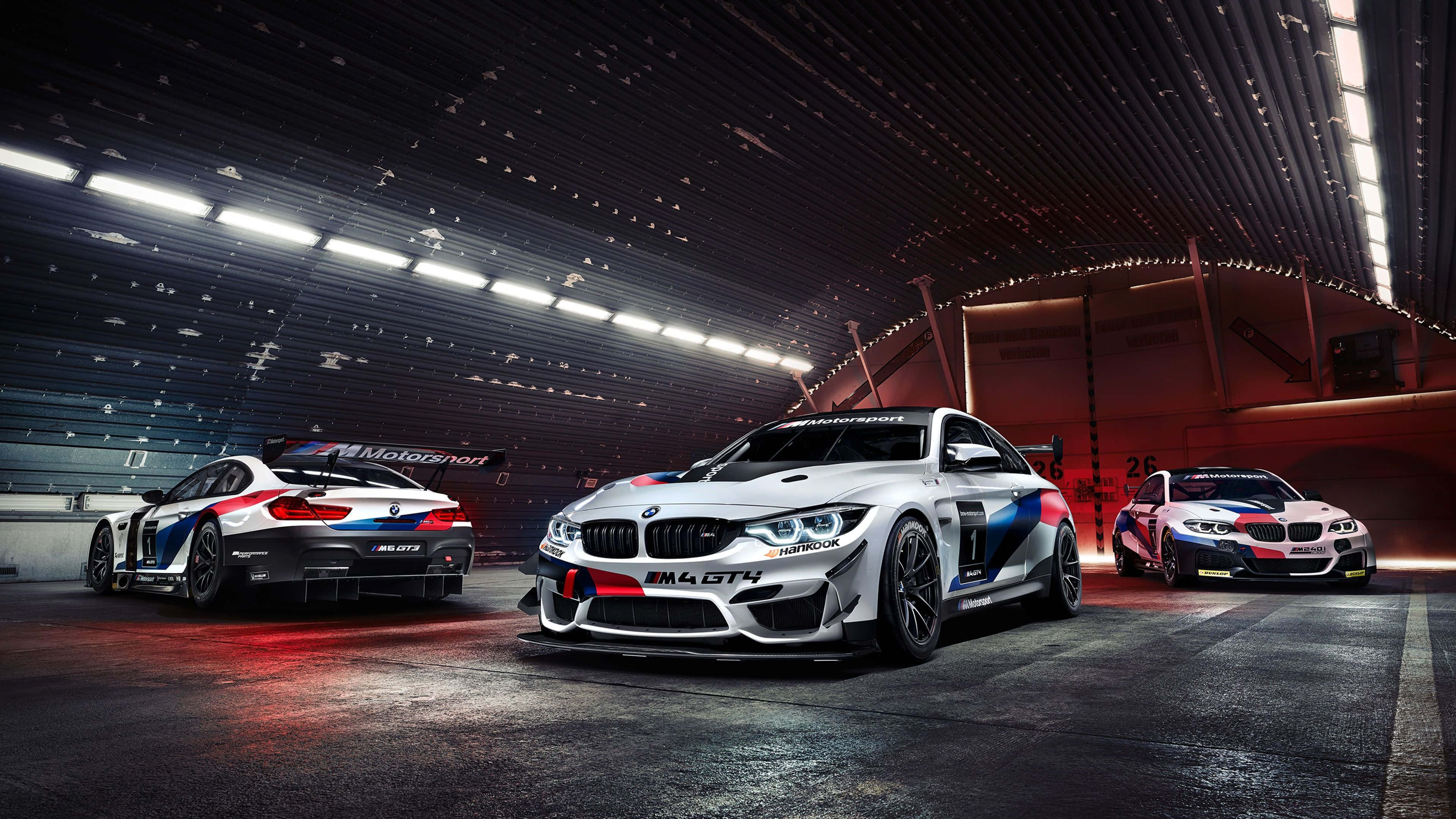 4K BMW 壁紙 桌布 壁紙 — 三輛BMW M4 GT4賽車在明亮的燈光下，在時尚的地下車庫中閃閃發光，地面濕潤反光。