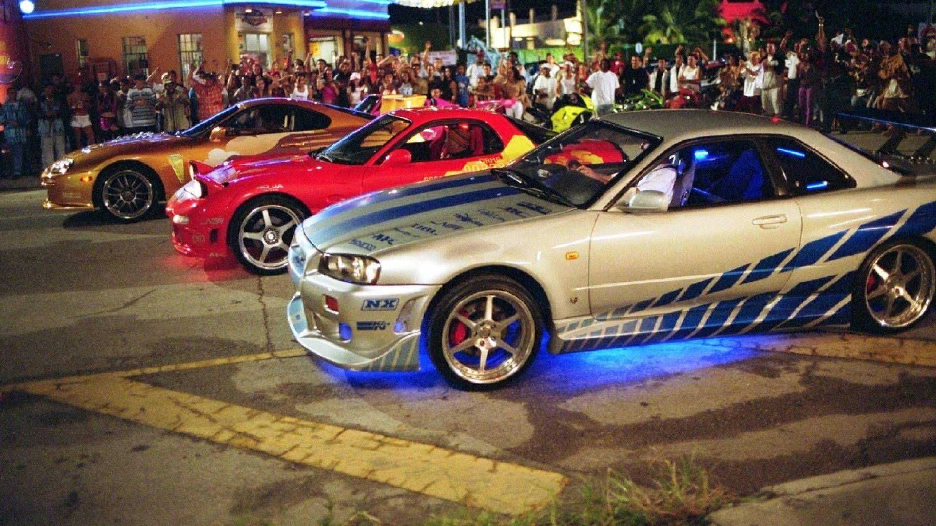fast 桌布 壁紙 — 三輛定制跑車在夜間停泊，帶有發光的底盤燈，吸引街上圍觀人群。