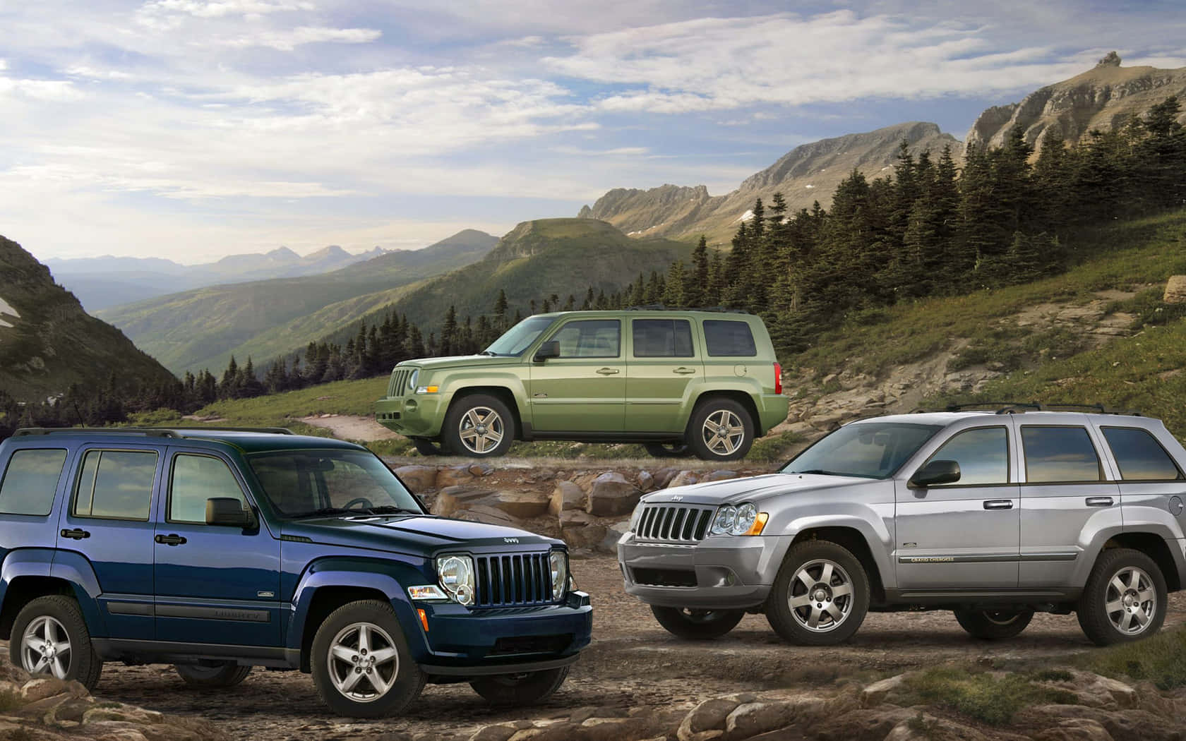 Jeep Liberty 桌布 壁紙 — 三輛藍色、綠色和銀色的Jeep SUV停泊在岩石地形上，背景是山脈，天空多雲。