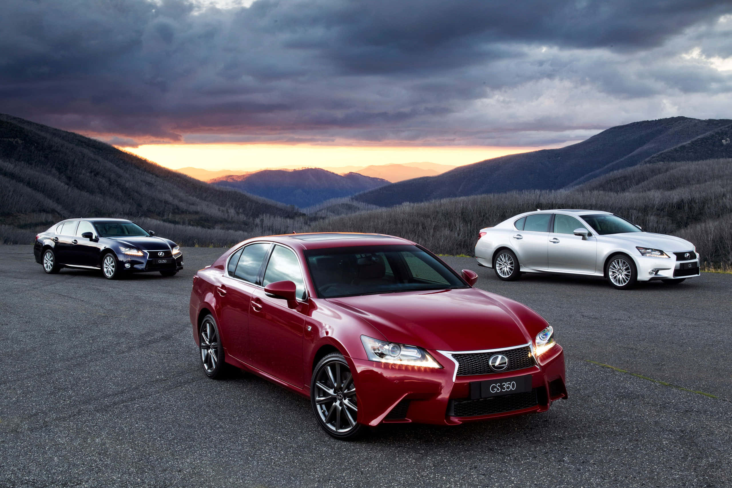 Lexus Gs 桌布 壁紙 — 三輛豪華轎車，紅色、黑色和銀色，停在山路上，夕陽西下，雲彩壯麗。