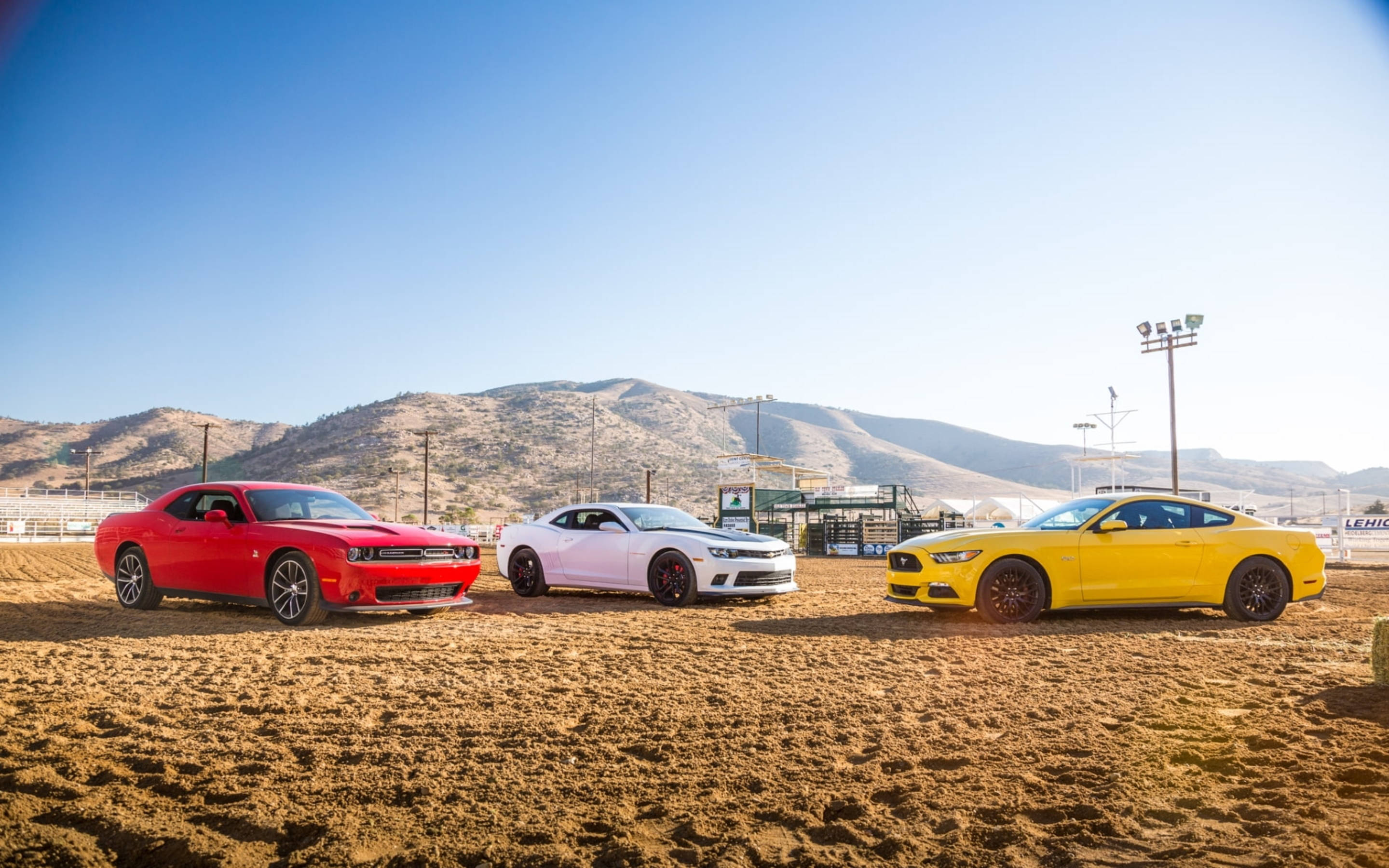Chevrolet 桌布 壁紙 — 三輛鮮豔的肌肉車紅色、白色和黃色停在一條泥濘的賽道上，背景是晴朗的藍天和山脈。