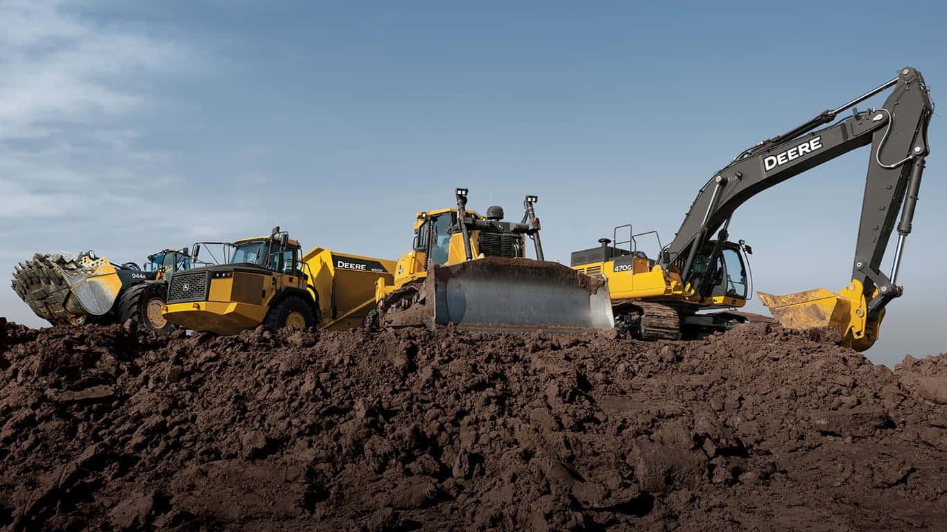 John Deere 桌布 壁紙 — 三輛黃色Deere工程車矗立在深色泥土堆上，背景是清澈的藍天。