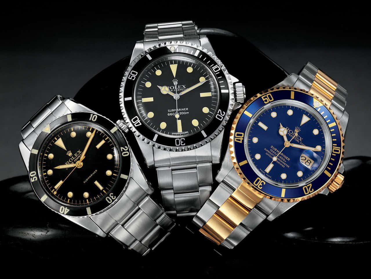 Rolex 桌布 壁紙 — 三隻奢華的勞力士Submariner手錶，配備黑色和藍色錶盤，在攝影棚燈光下於深色反光表面上閃耀。